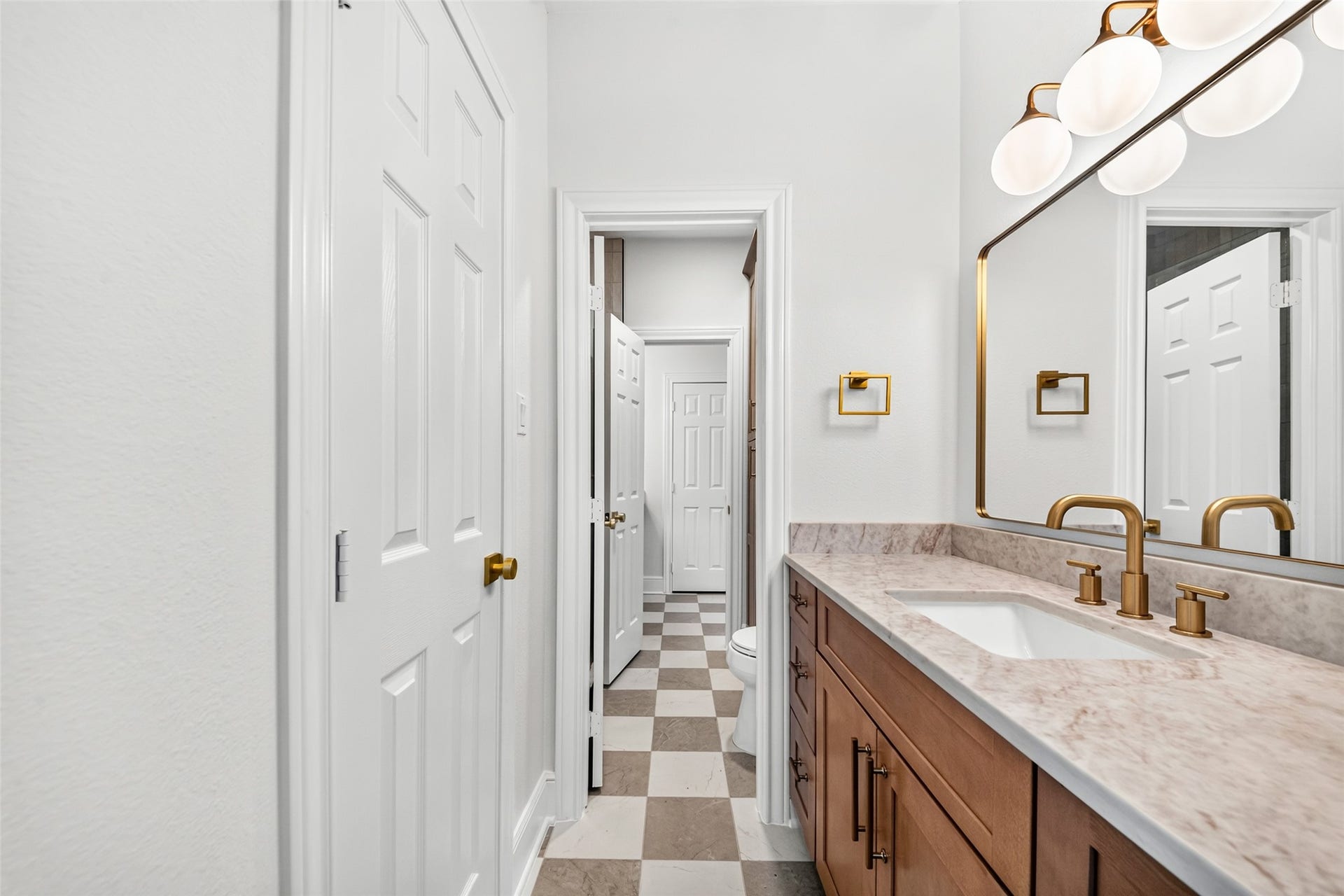 46 Pebble Cove Drive, The Woodlands, TX 77381 Elegant bathroom with a spacious marble-topped vanity, modern brass fixtures, and stylish checkerboard flooring, creating a luxurious and inviting atmosphere.
