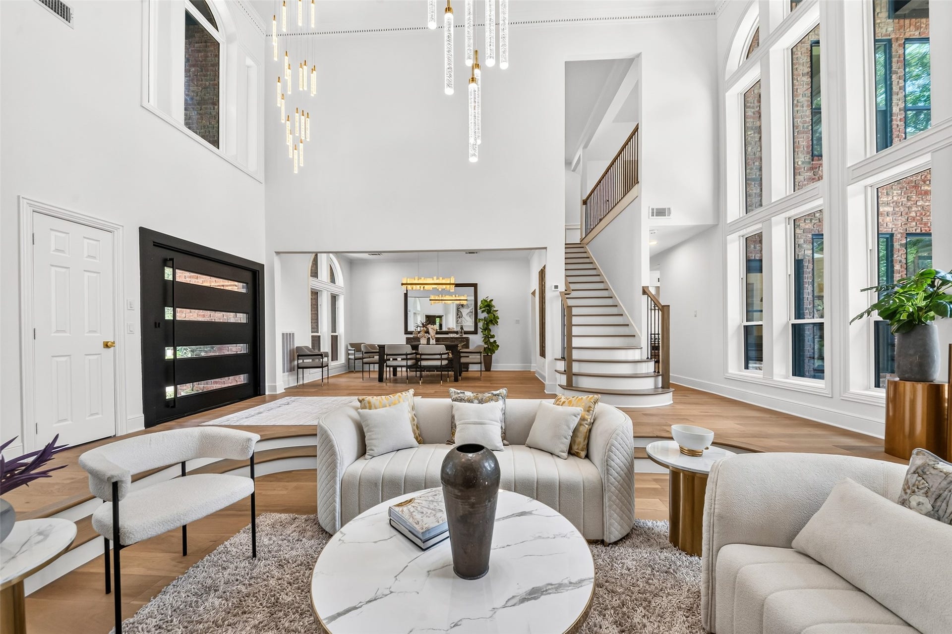 46 Pebble Cove Drive, The Woodlands, TX 77381 Stunning open-concept living area with soaring ceilings, elegant chandelier, and expansive windows that flood the space with natural light. A graceful staircase leads to the upper level, while modern finishes and luxurious seating create a sophisticated ambiance.
