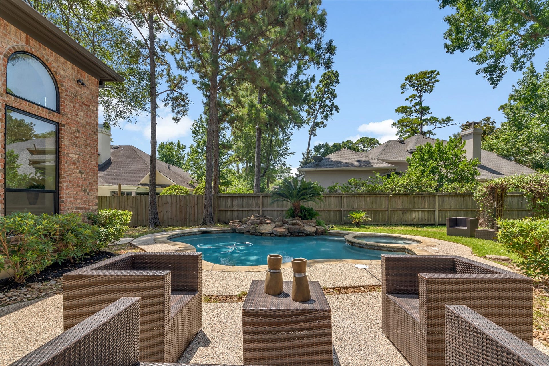46 Pebble Cove Drive, The Woodlands, TX 77381 Tranquil backyard oasis featuring a sparkling pool, spa, and stylish outdoor seating surrounded by lush greenery and tall trees for added privacy.