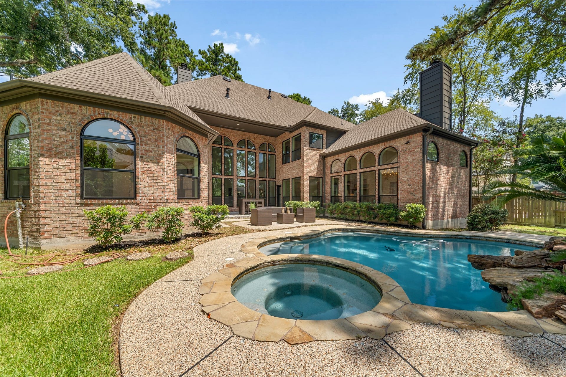 46 Pebble Cove Drive, The Woodlands, TX 77381 Stunning brick home featuring a spacious backyard with a luxurious pool and spa, surrounded by lush greenery and elegant landscaping.