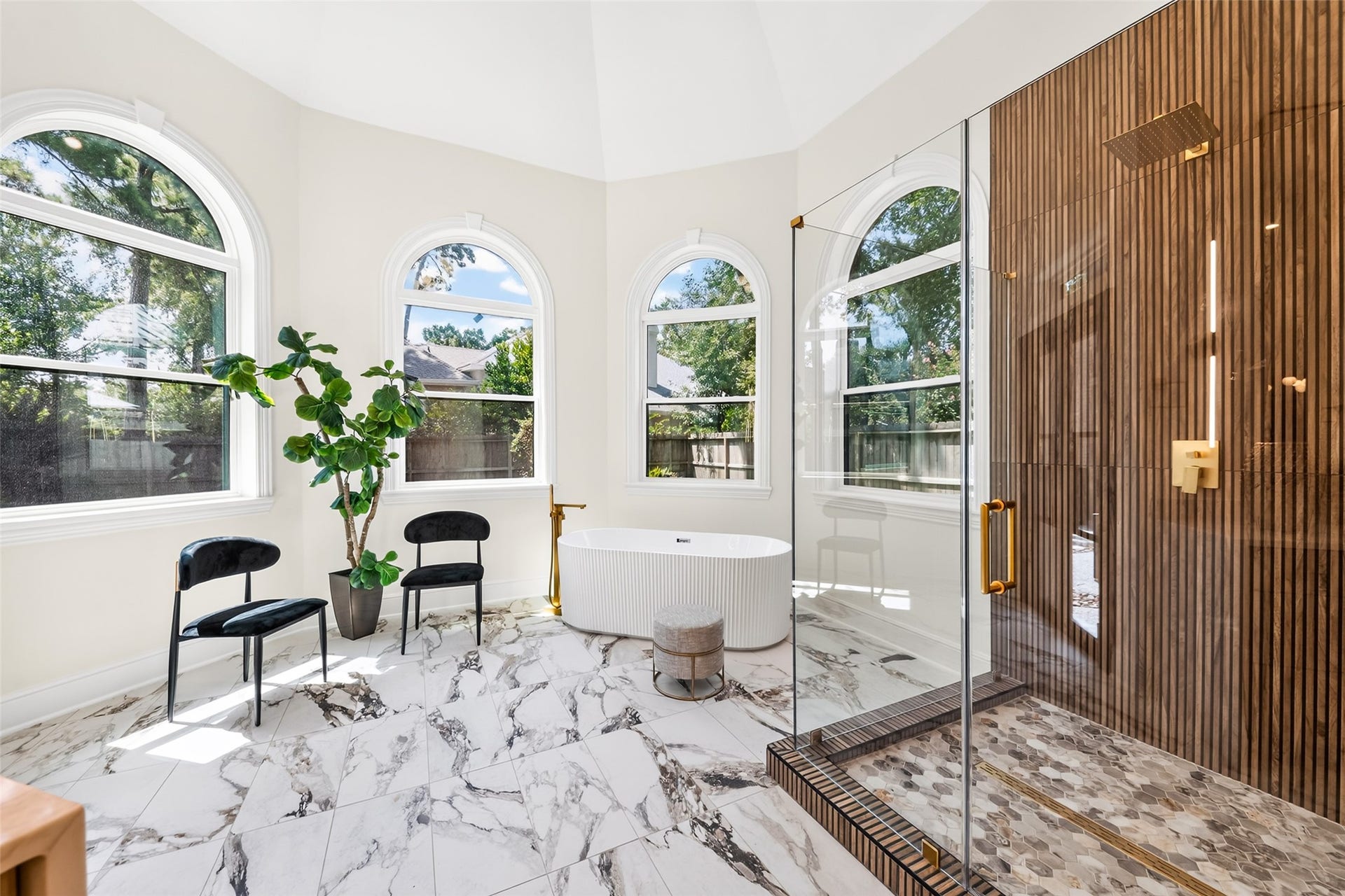 46 Pebble Cove Drive, The Woodlands, TX 77381 Bright and elegant bathroom featuring a luxurious walk-in shower with wood panel accents, a stand-alone tub, and large arched windows offering serene garden views.