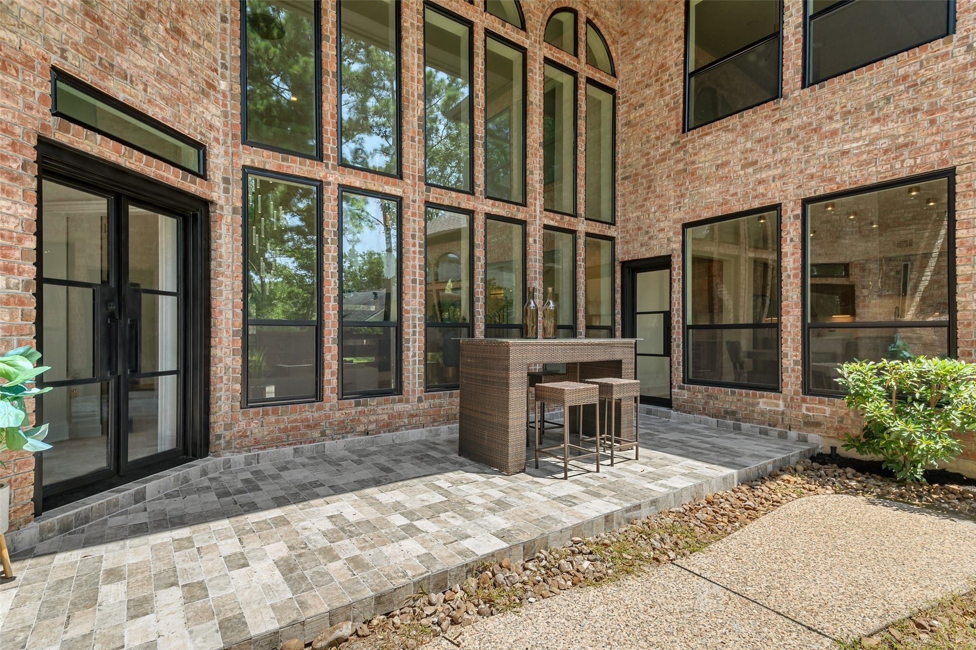46 Pebble Cove Drive, The Woodlands, TX 77381 Expansive brick patio with towering windows offers a perfect blend of natural light and outdoor charm, ideal for entertaining or relaxing.