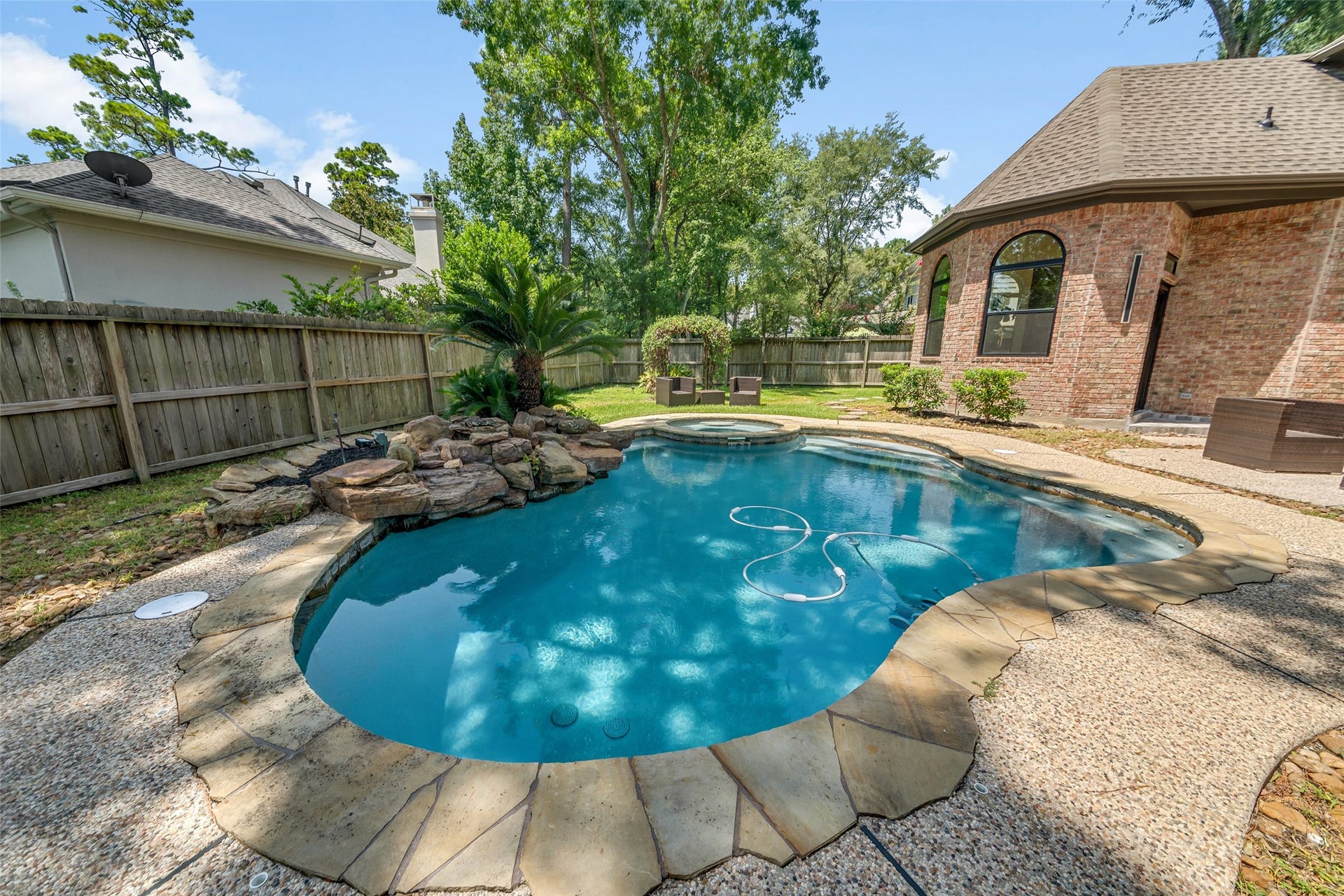 46 Pebble Cove Drive, The Woodlands, TX 77381 Experience the perfect outdoor retreat with this stunning backyard featuring a sparkling pool surrounded by lush greenery and a charming stone waterfall. Ideal for relaxation and entertaining.