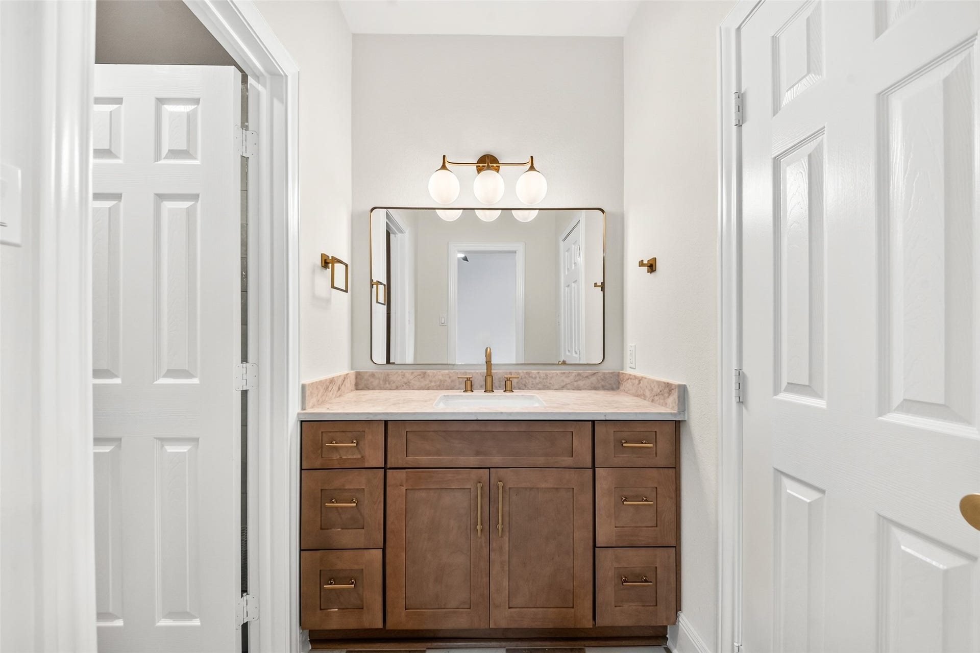 46 Pebble Cove Drive, The Woodlands, TX 77381 Elegant bathroom featuring a warm wood vanity with brass hardware, complemented by a sleek countertop and modern lighting.