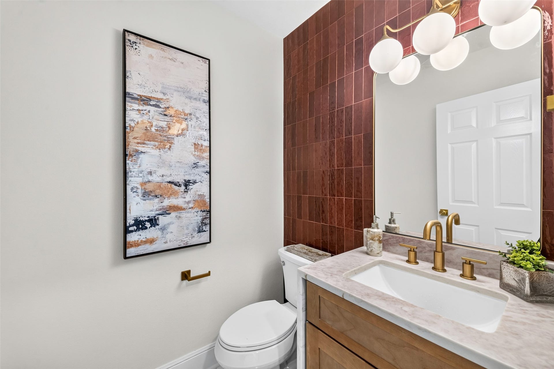 46 Pebble Cove Drive, The Woodlands, TX 77381 Chic and modern, this downstairs half bath features elegant gold fixtures, a striking tile accent wall, and contemporary art, creating a stylish and inviting space.
