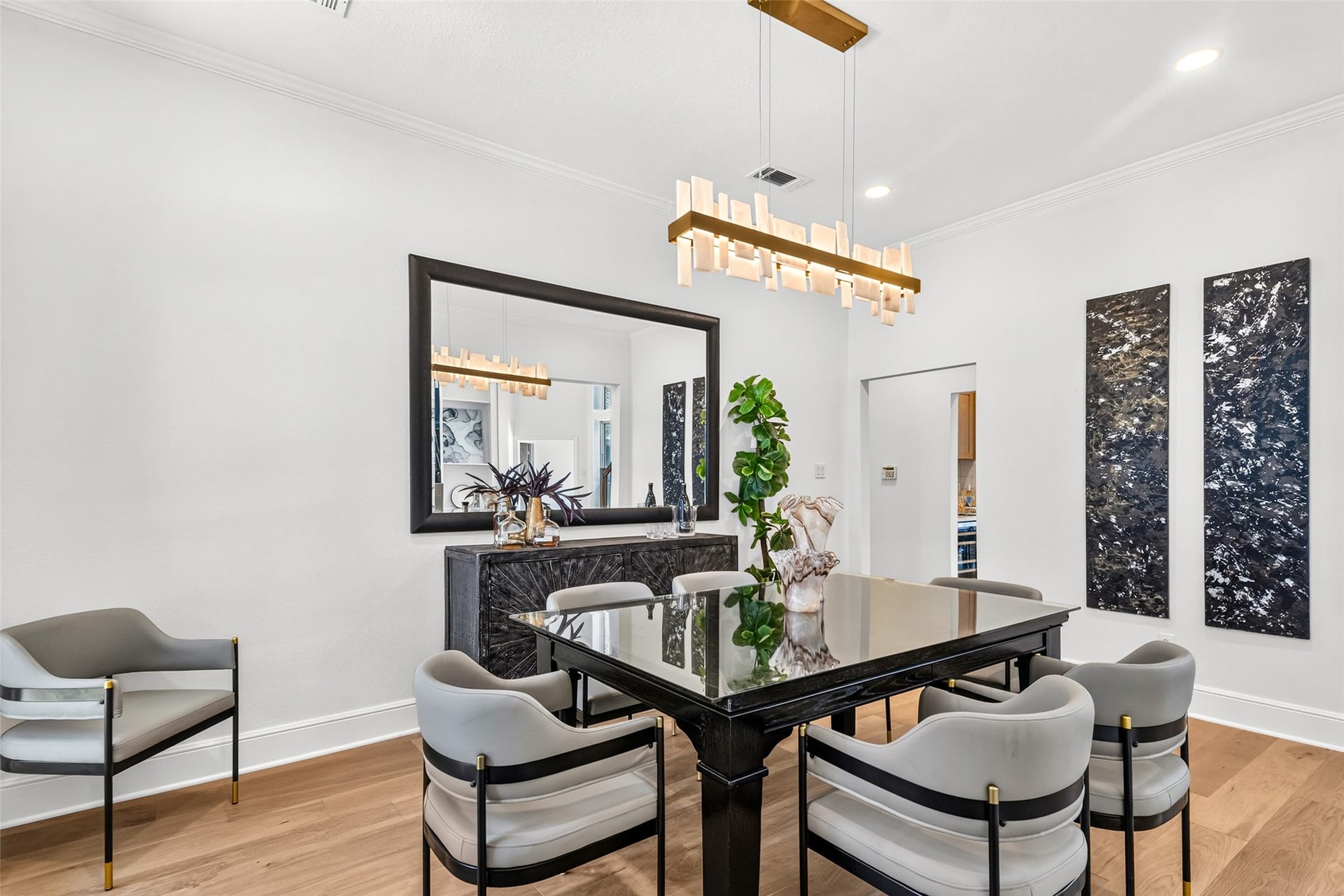 46 Pebble Cove Drive, The Woodlands, TX 77381 Elegant dining area featuring a sleek black table, modern chairs, and contemporary art. A chic chandelier and large mirror enhance the space, creating a stylish and inviting atmosphere.