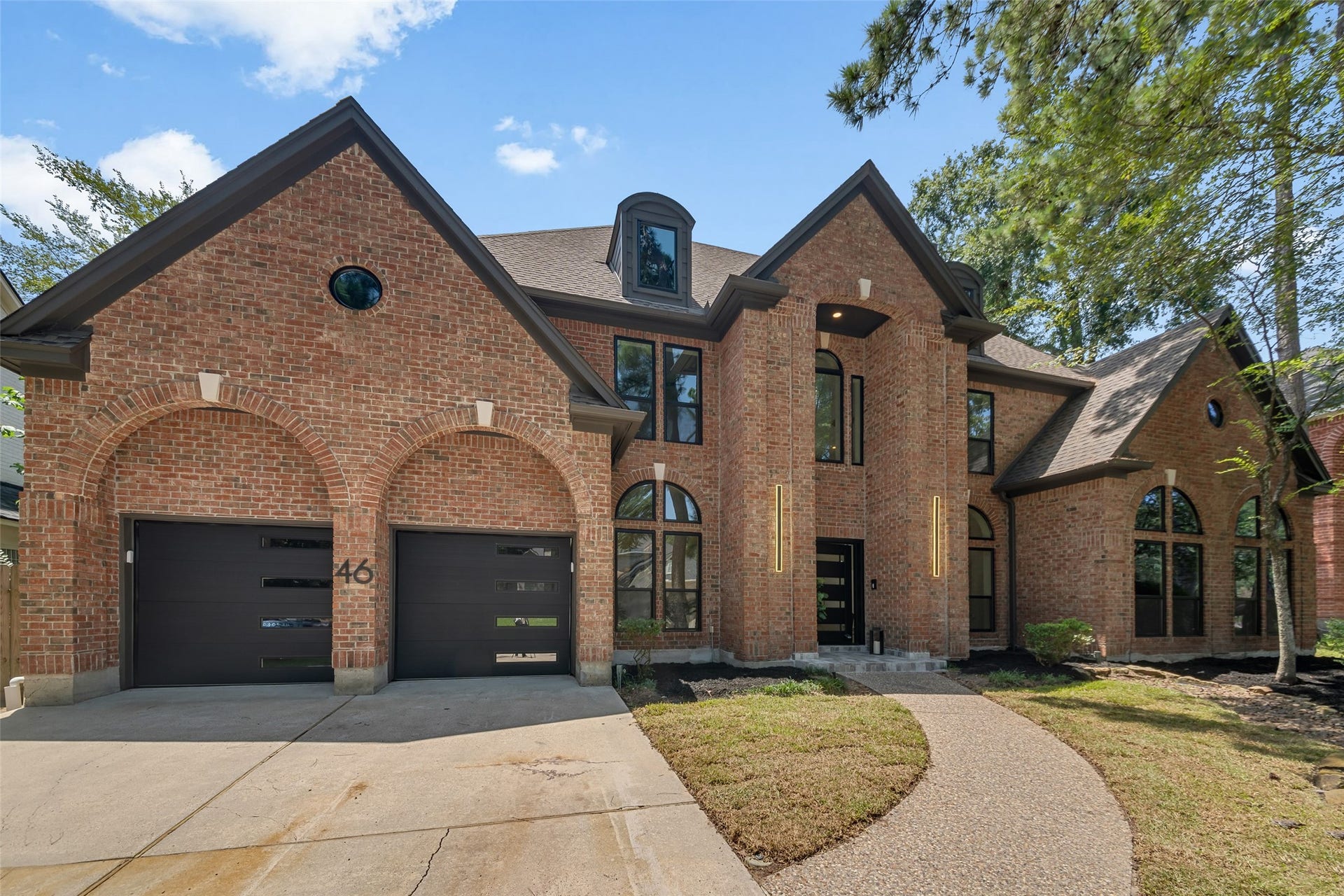 46 Pebble Cove Drive, The Woodlands, TX 77381 Stunning brick home with elegant arched windows, a modern double garage, and a welcoming curved pathway set amidst mature trees.