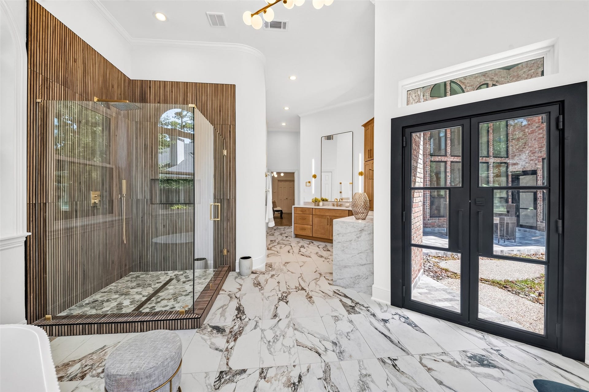 46 Pebble Cove Drive, The Woodlands, TX 77381 Luxurious bathroom with elegant marble flooring, a spacious glass-enclosed shower, and double vanity. The room is enhanced by large windows and a modern black-framed entrance, seamlessly connecting to an outdoor patio.