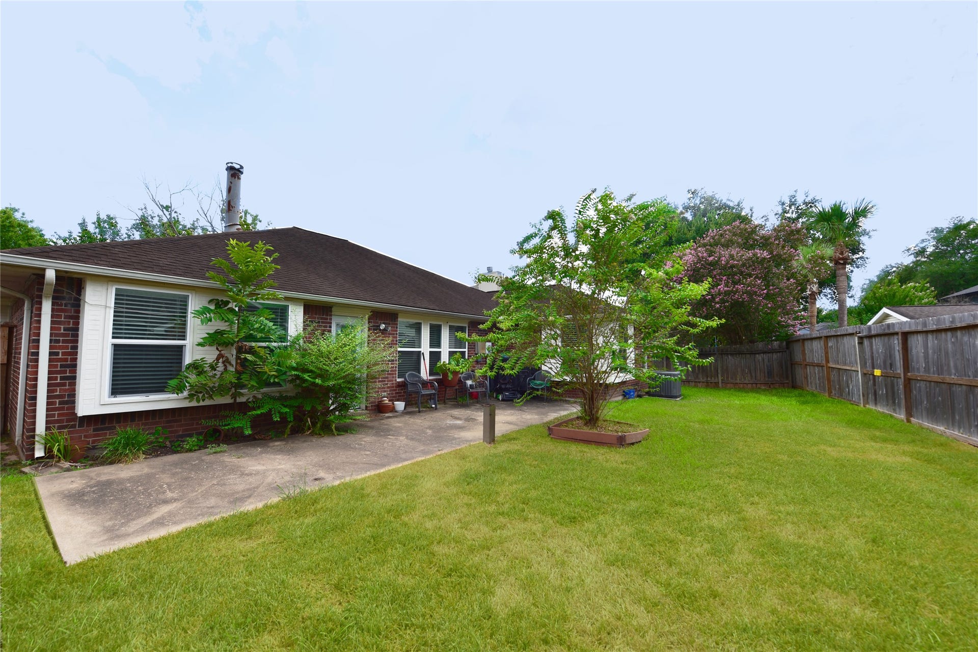 3411 Cannon Ridge Drive, Richmond, TX 77406 This photo shows a cozy backyard with a brick house, patio area, and mature landscaping. The yard is fenced, offering privacy and space for outdoor activities.