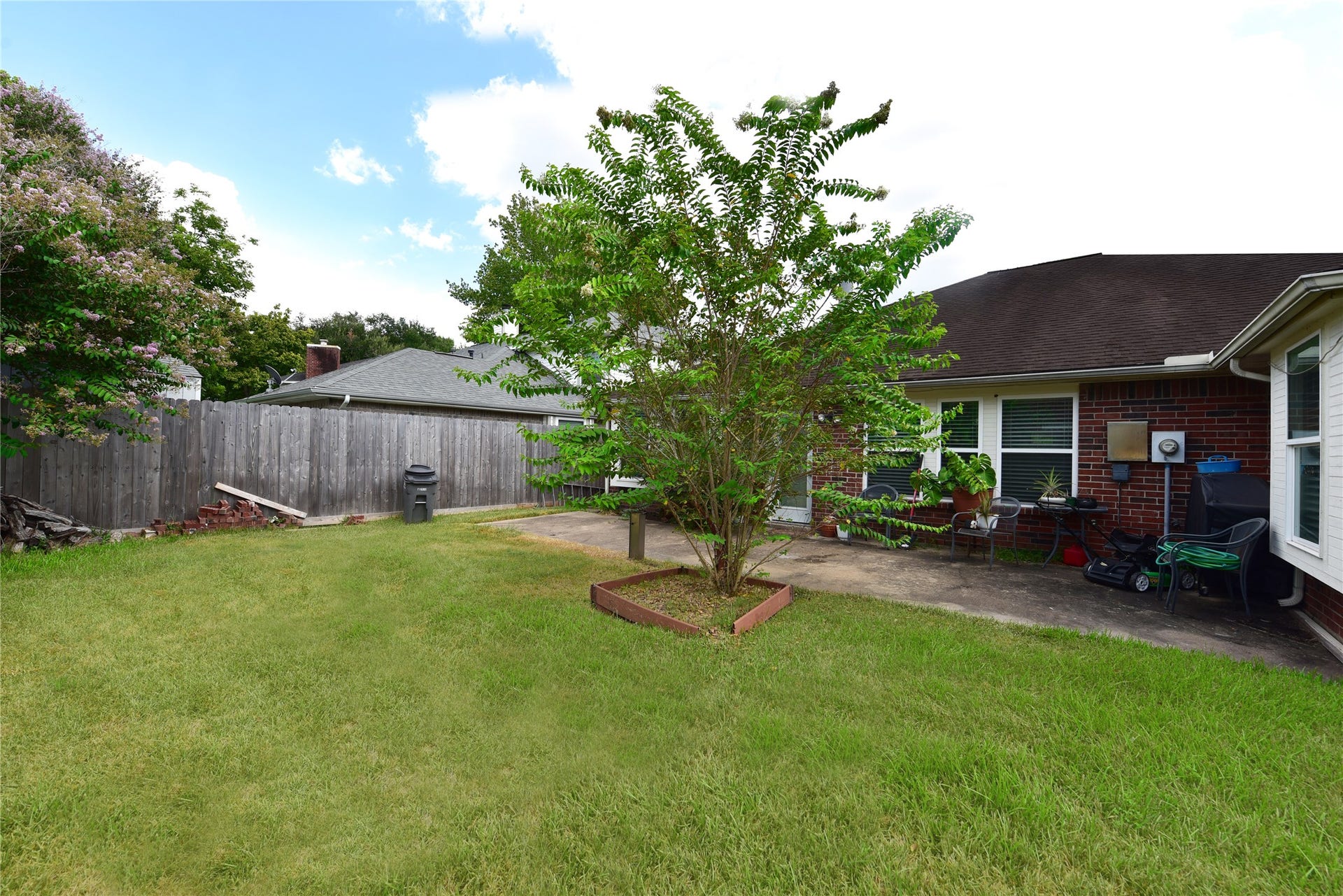 3411 Cannon Ridge Drive, Richmond, TX 77406 This backyard features a spacious lawn with a central tree, a patio area adjacent to a brick house, and a wooden fence for privacy. Ideal for outdoor activities and relaxation.