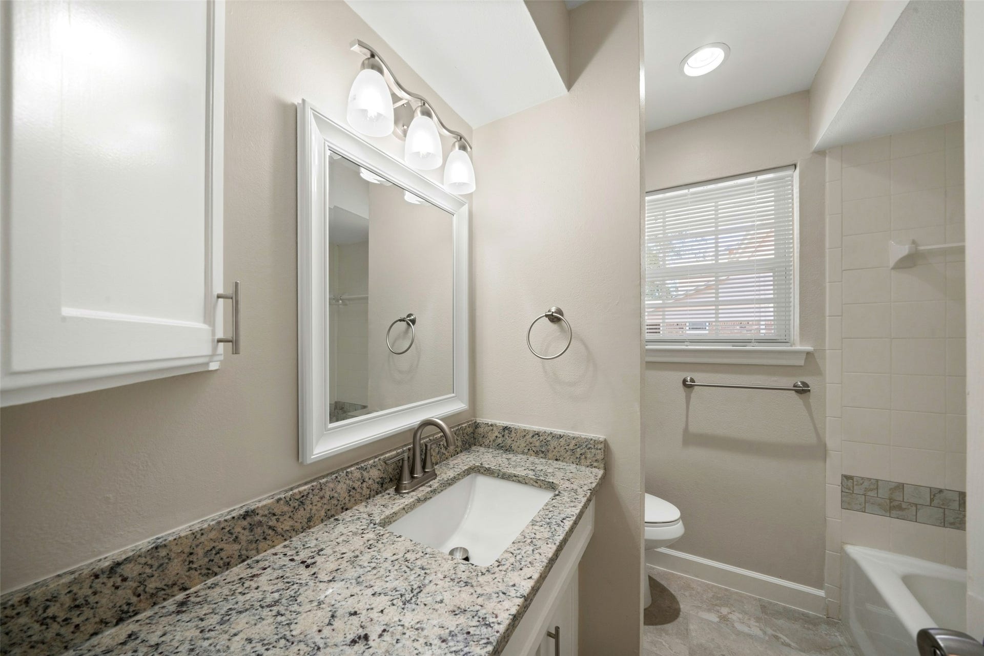 3402 Dovie Drive, Spring, TX 77380 This bright, updated hall bathroom features a clean neutral color palette, a new granite countertop, an undermount sink with brushed nickel faucet, and a crisp white-framed mirror that adds a fresh, polished look. The space is finished with coordinating brushed nickel fixtures, ample lighting, and a tiled tub/shower area for a clean and timeless feel.