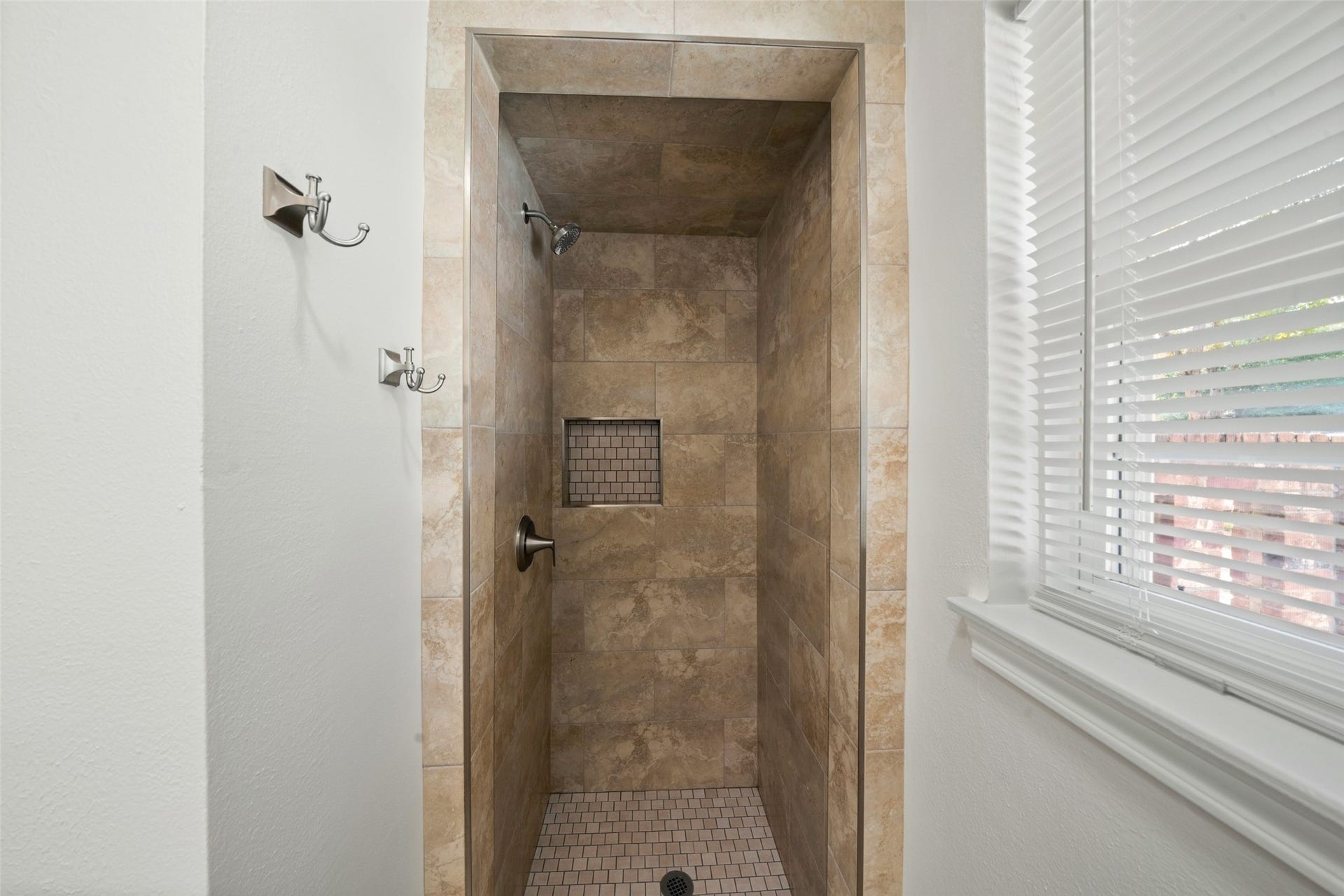 3402 Dovie Drive, Spring, TX 77380 This updated primary bathroom features a newly tiled walk-in shower with warm neutral tones, a built-in recessed niche for added convenience, and coordinating tile flooring for a clean, finished look. The shower is complemented by brushed nickel faucets and fixtures, creating a polished, modern feel while maintaining a warm and timeless design.