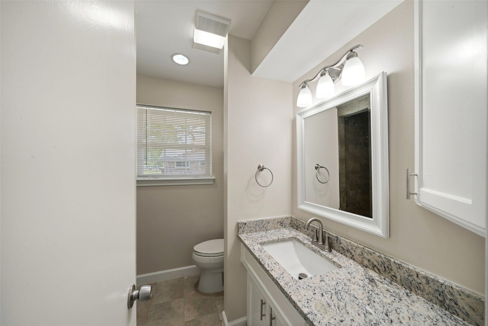 3402 Dovie Drive, Spring, TX 77380 This bright and refreshed primary bathroom features a clean, neutral design with a spacious vanity and plenty of natural light. The vanity has been updated with newly installed Dallas White granite countertops, complemented by brushed nickel faucets and fixtures for a modern finish. A large white-framed mirror and coordinated lighting complete the polished, updated look.