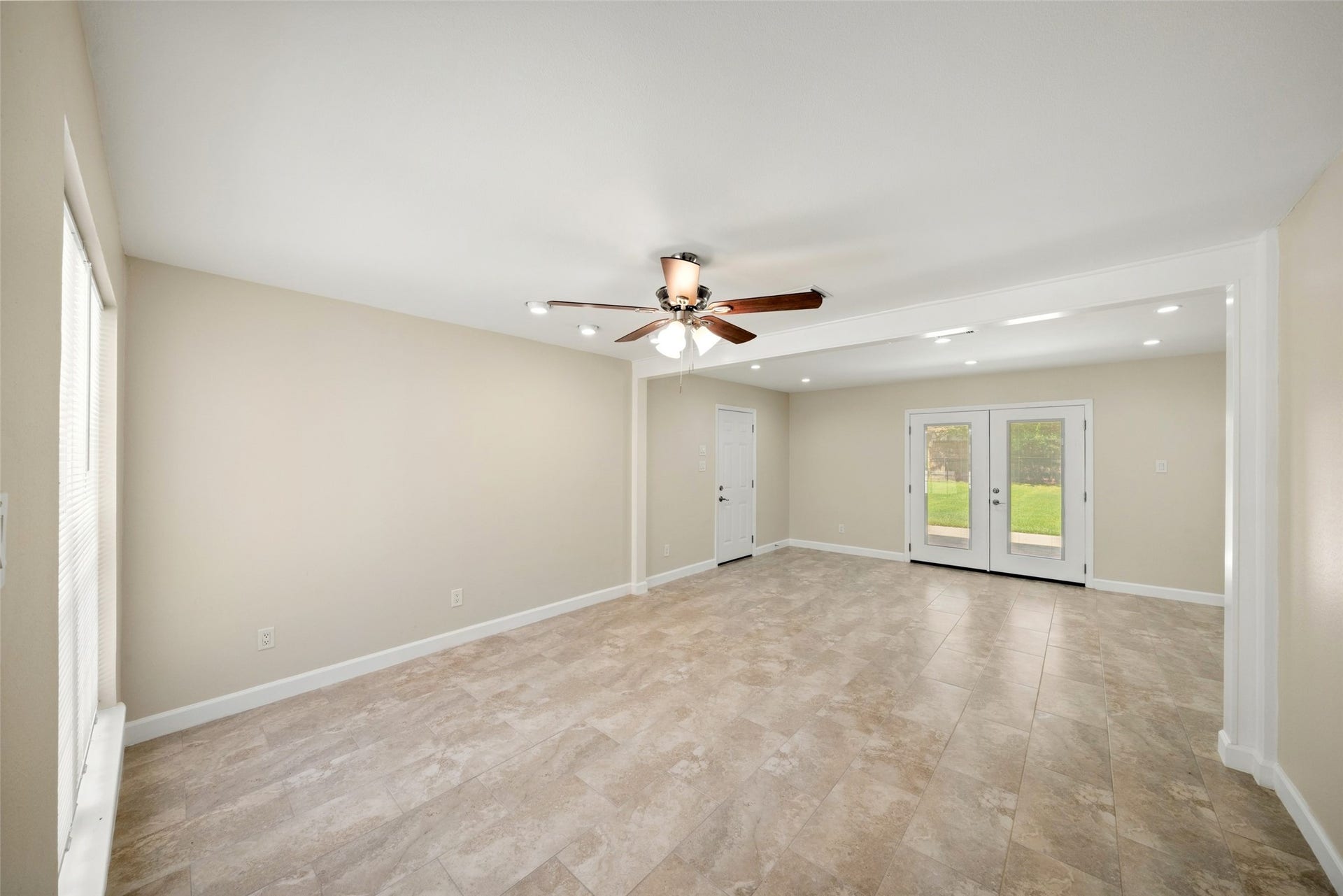 3402 Dovie Drive, Spring, TX 77380 This spacious living room offers a bright, open layout with plenty of flexibility for multiple furniture arrangements and entertaining. Modelo Beige Matte II ceramic tile has been installed throughout, creating a clean and cohesive look. The walls, ceilings, and baseboards have all been freshly painted, giving the space a crisp, move-in-ready finish. Recessed lighting, a ceiling fan, and French doors overlooking the backyard add to the rooms bright and welcoming feel.