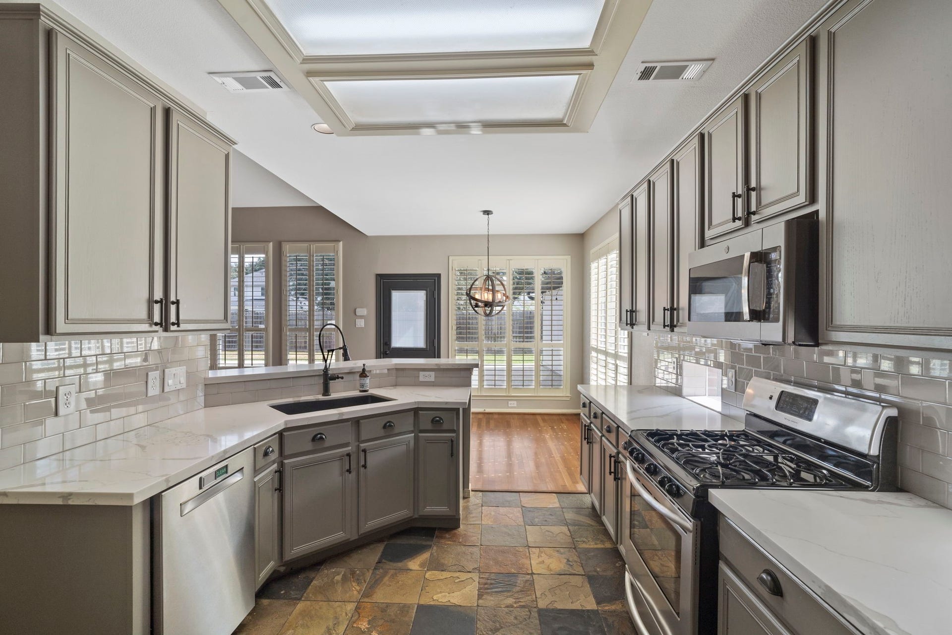 9730 Harrison Lane, Missouri City, TX 77459 Gourmet kitchen perspective showcasing updated soft sage cabinetry, bright quartz counter surfaces, white subway tile backsplash, stainless gas appliances, natural slate tile flooring, and recessed ceiling lighting.