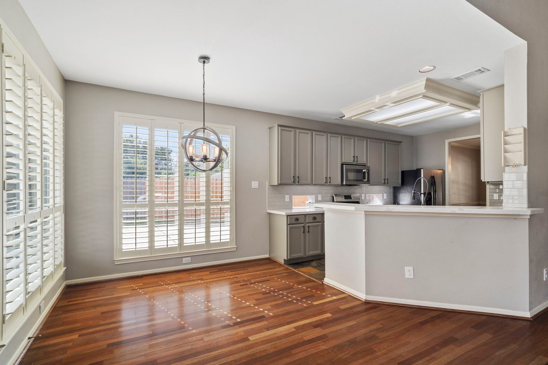 9730 Harrison Lane, Missouri City, TX 77459 Sunlit breakfast nook featuring rich wood-look flooring, spherical metal chandelier, perimeter windows with custom plantation shutters, and clear line of sight to the updated kitchen.