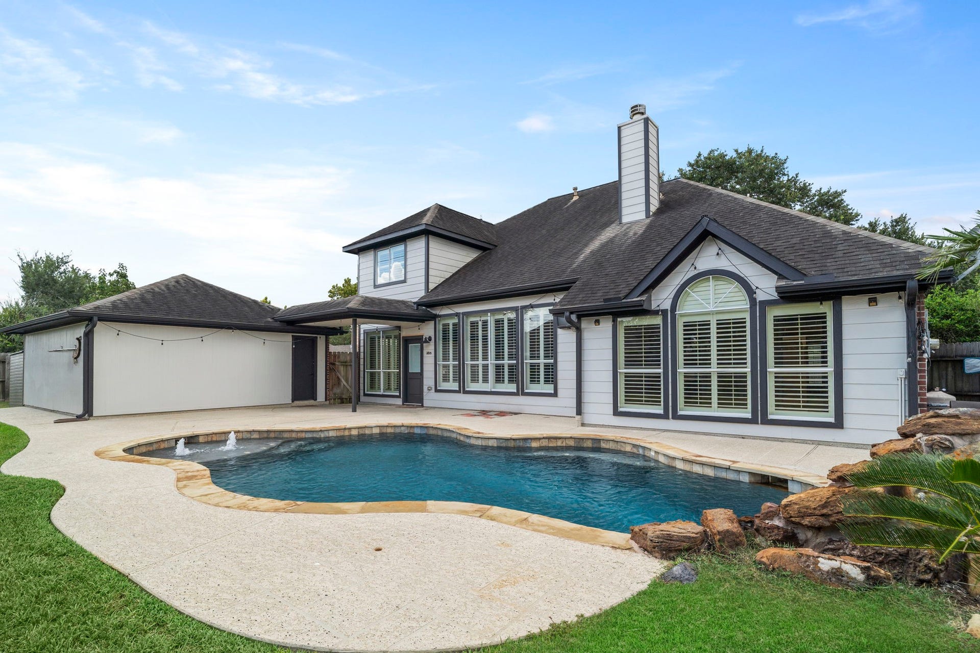 9730 Harrison Lane, Missouri City, TX 77459 Private backyard oasis highlighting the custom in-ground swimming pool with water fountains, rock waterfall feature, and surrounding cool-deck patio.