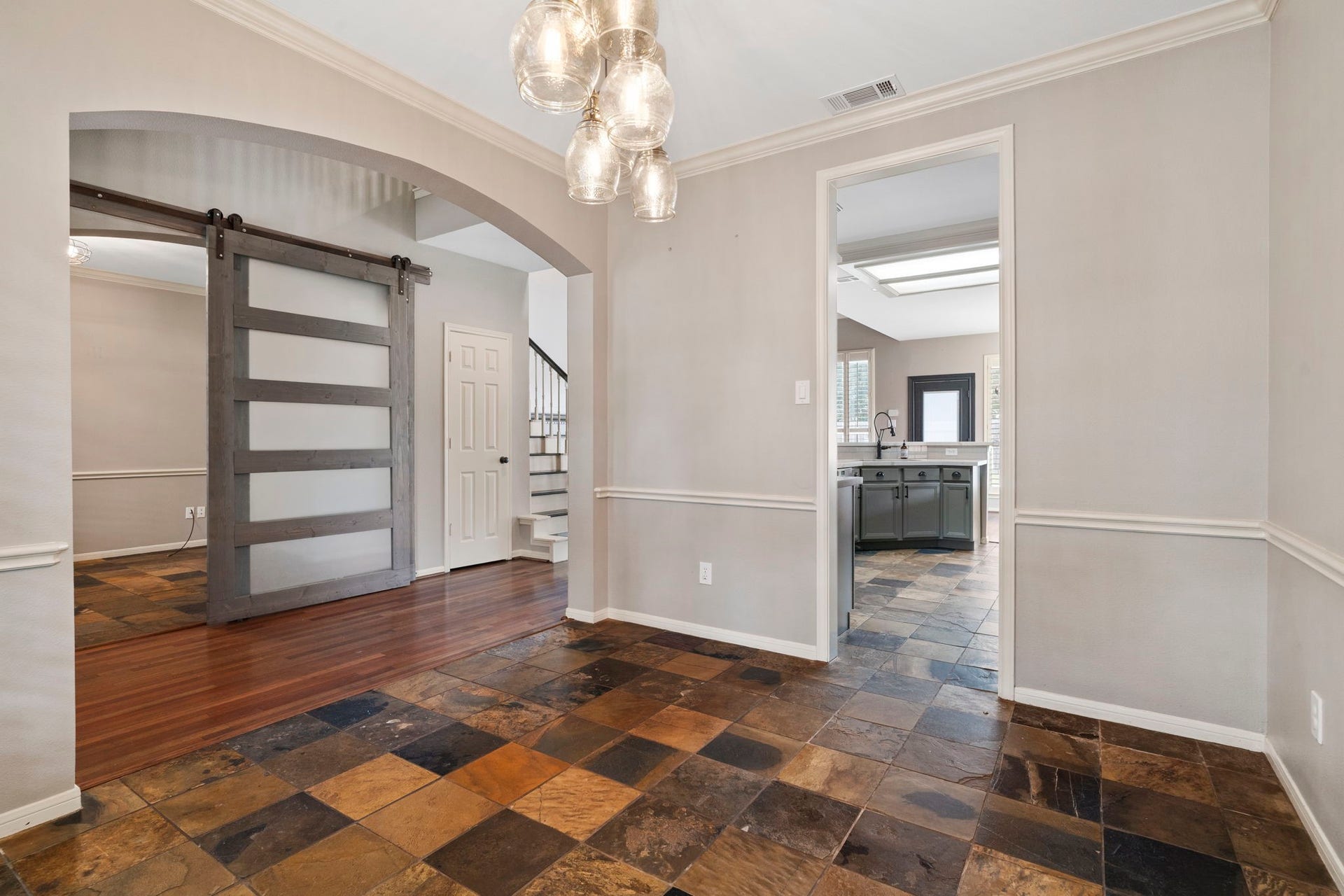 9730 Harrison Lane, Missouri City, TX 77459 Spacious formal dining area view showing open archways leading to the kitchen and front entry hall, accented by slate tile flooring and custom glass barn doors.