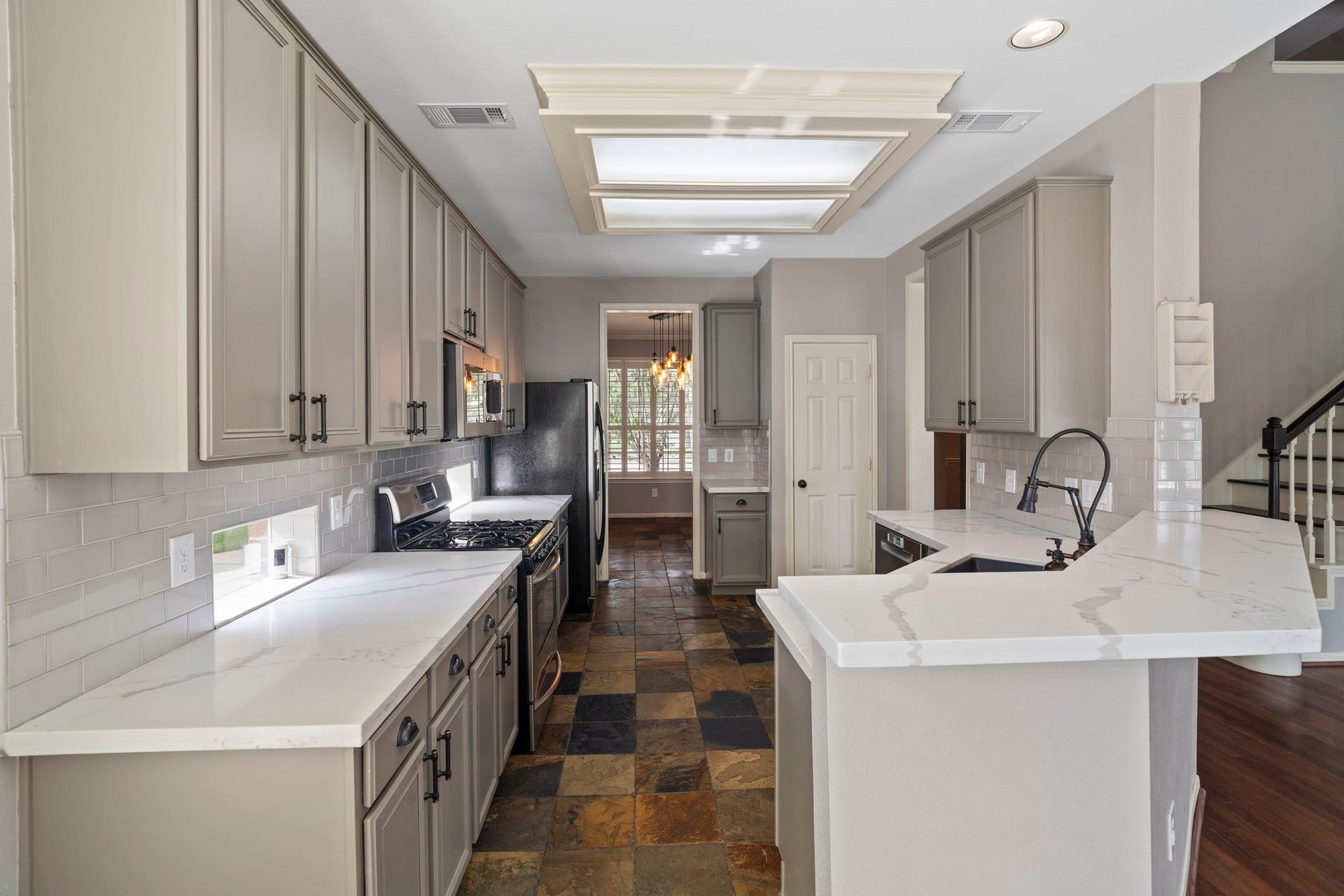 9730 Harrison Lane, Missouri City, TX 77459 Full galley view of the updated gourmet kitchen highlighting the extensive quartz workspace, natural slate tile flooring, soft sage cabinetry, subway tile backsplash, and raised breakfast bar barstool seating ledge.