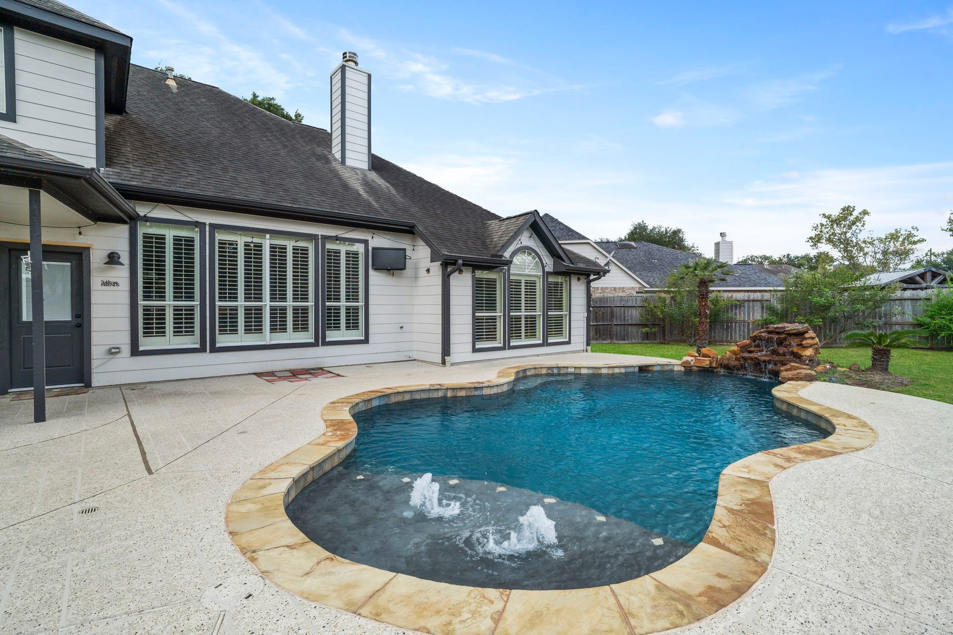 9730 Harrison Lane, Missouri City, TX 77459 Overview of the resort-style pool setup displaying the stone rock waterfall, decorative water features, and ample outdoor patio lounge space.