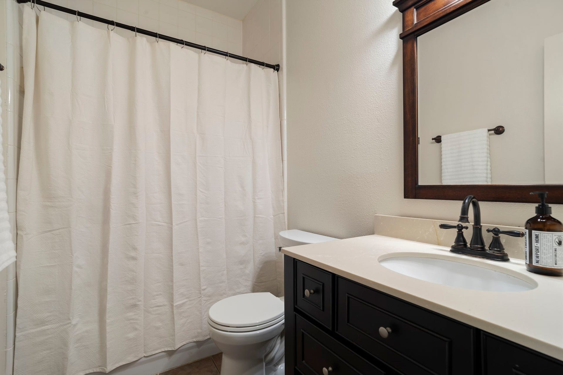 9730 Harrison Lane, Missouri City, TX 77459 Full ground-floor bathroom showcasing a dark wood vanity cabinet, warm solid countertop, oil-rubbed bronze plumbing fixtures, frame-matching mirror, and tile flooring.