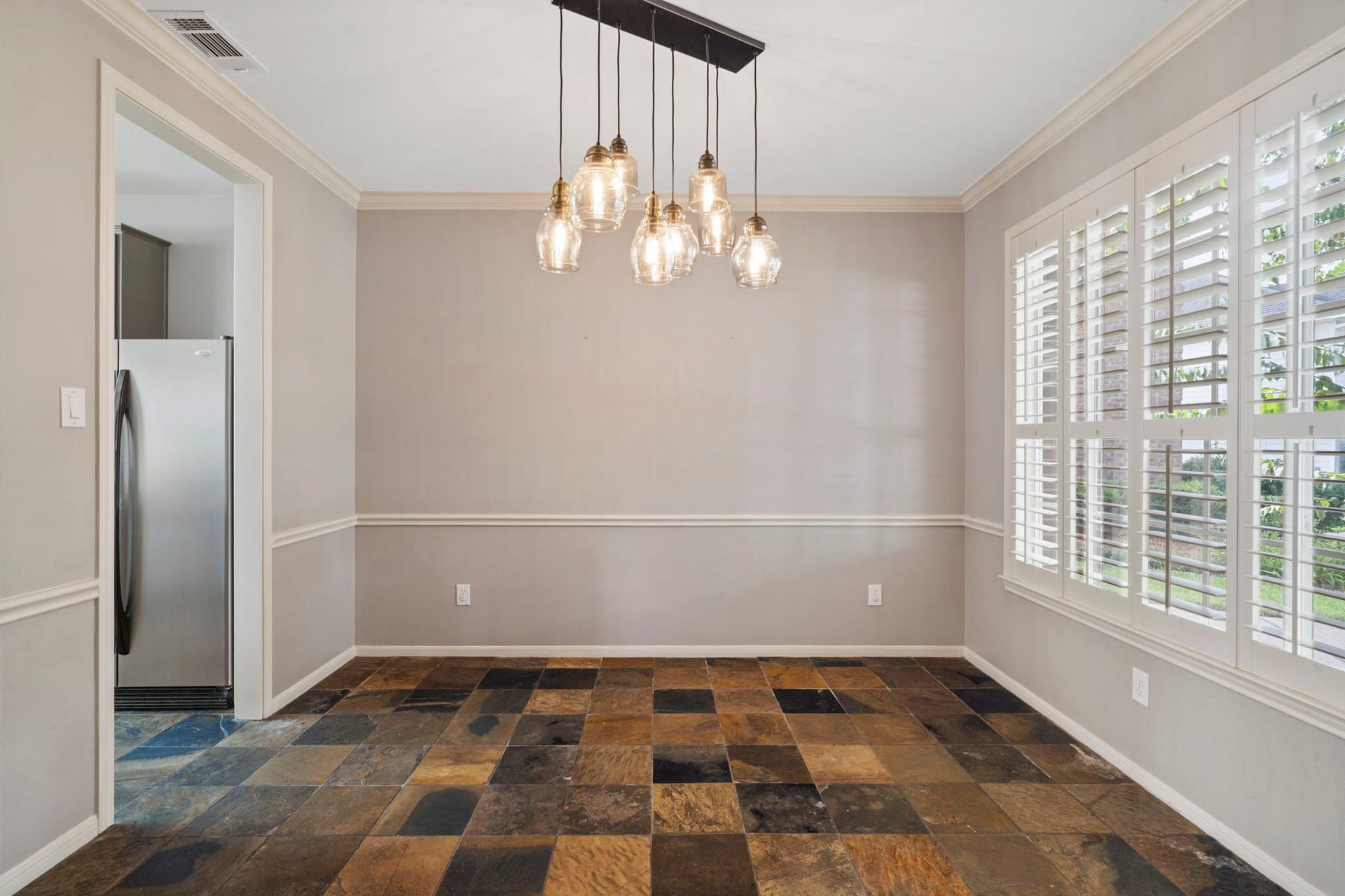 9730 Harrison Lane, Missouri City, TX 77459 Formal dining room showcasing natural slate tile flooring, elegant glass-globe multi-light chandelier fixture, custom plantation window shutters, and classic wall chair rail detailing.