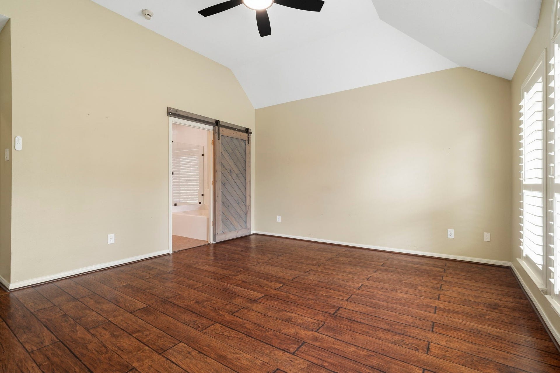 9730 Harrison Lane, Missouri City, TX 77459 Spacious primary suite featuring soaring vaulted ceilings, dark wood-look flooring, ceiling fan, and a rustic sliding barn door opening directly to the en-suite bathroom.