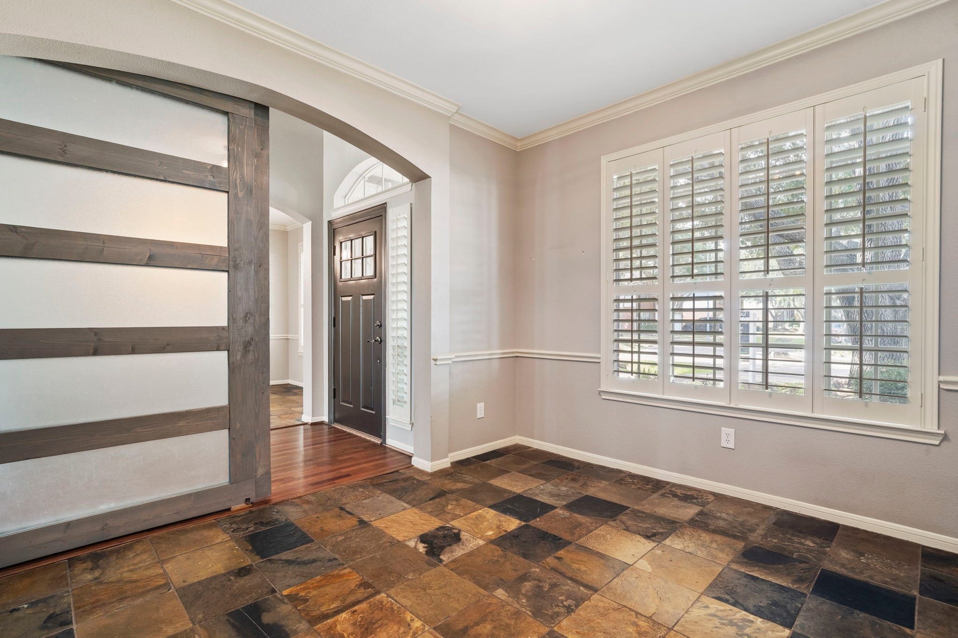 9730 Harrison Lane, Missouri City, TX 77459 Secondary entrance angle highlighting the low-maintenance natural slate tile flooring, custom wall chair rail molding, shuttered windows, and dark sliding frosted glass barn door.