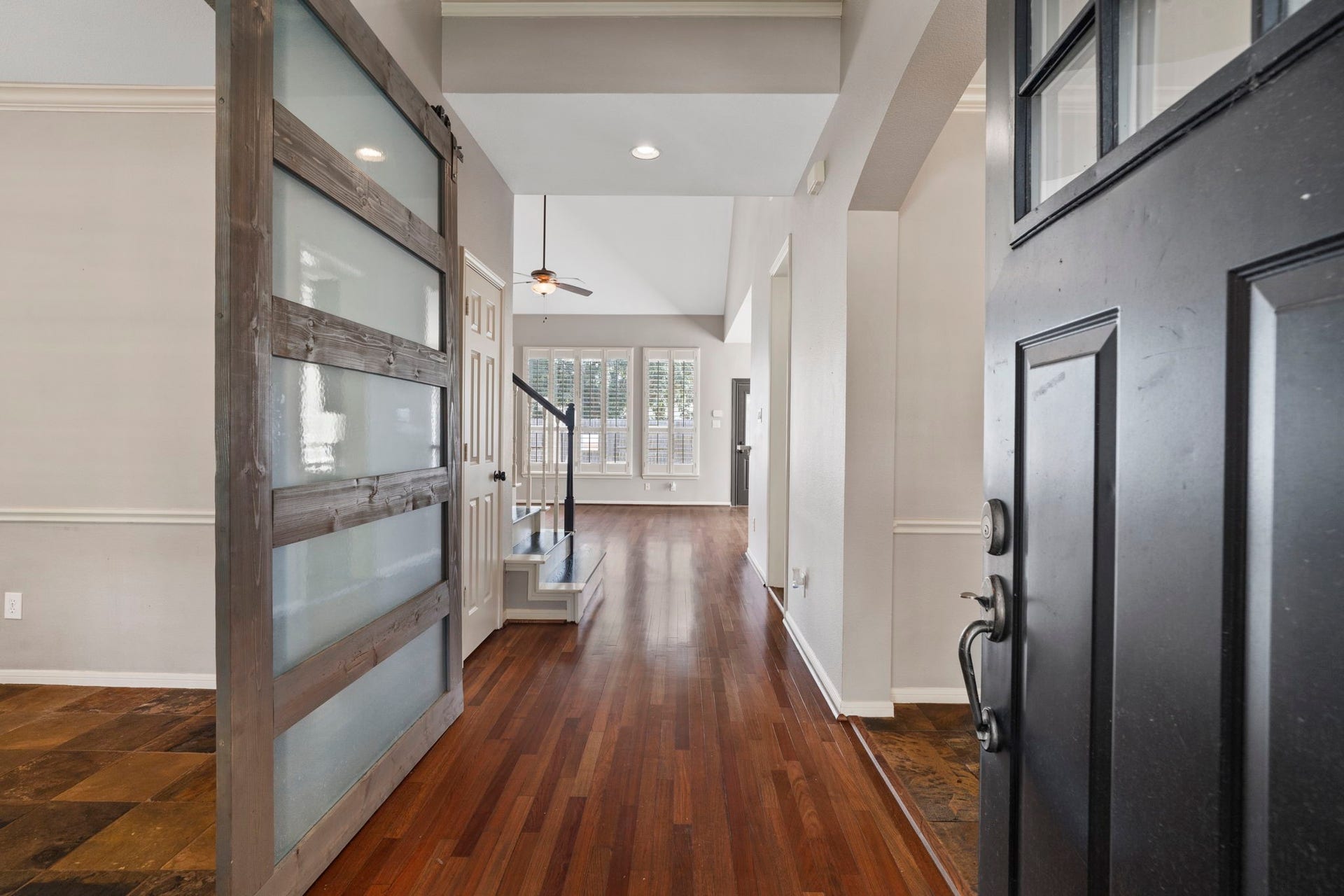 9730 Harrison Lane, Missouri City, TX 77459 Dramatic grand entryway framed by a heavy solid-wood front door, rich wood-look floors extending down the long foyer, and sliding frosted glass barn door accenting the adjacent flex room.