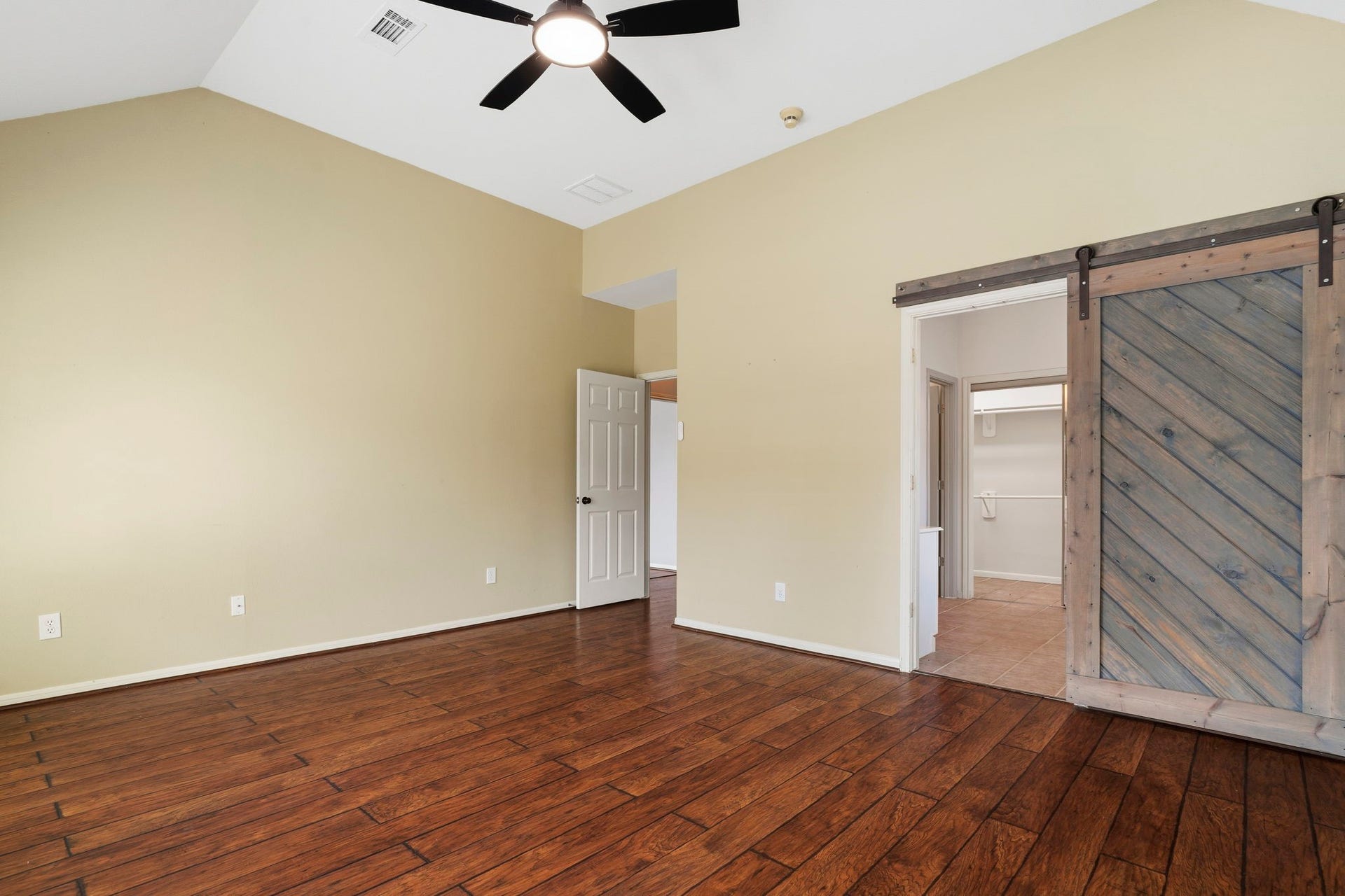 9730 Harrison Lane, Missouri City, TX 77459 Primary suite highlight showing the impressive vaulted ceiling height and rustic sliding wooden barn door leading into the en-suite primary bath.