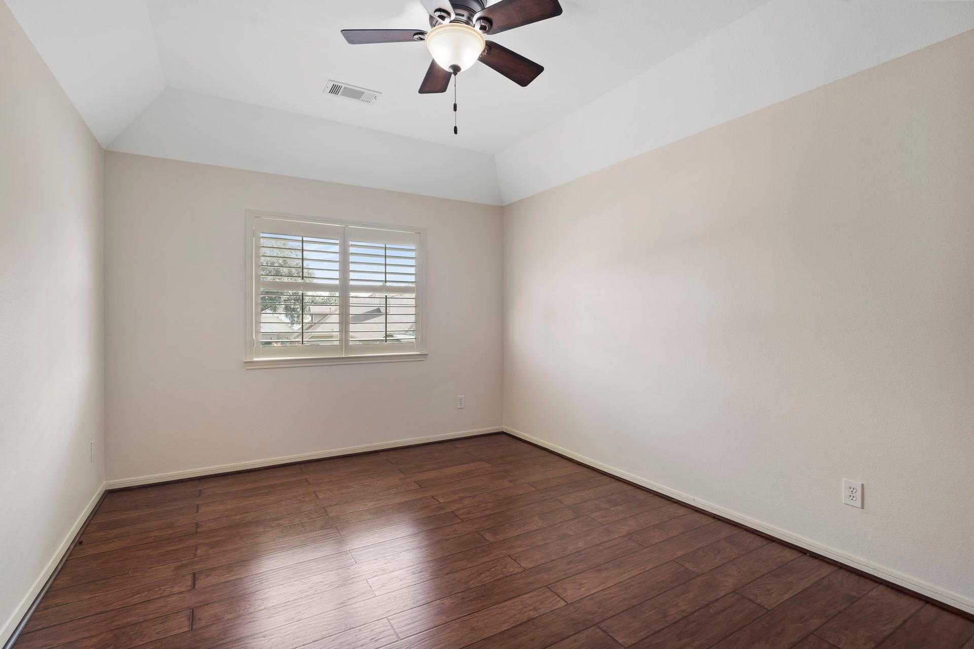 9730 Harrison Lane, Missouri City, TX 77459 Spacious secondary bedroom featuring wood-look LVP flooring, custom plantation window shutters, a ceiling fan, and high vaulted ceiling details.