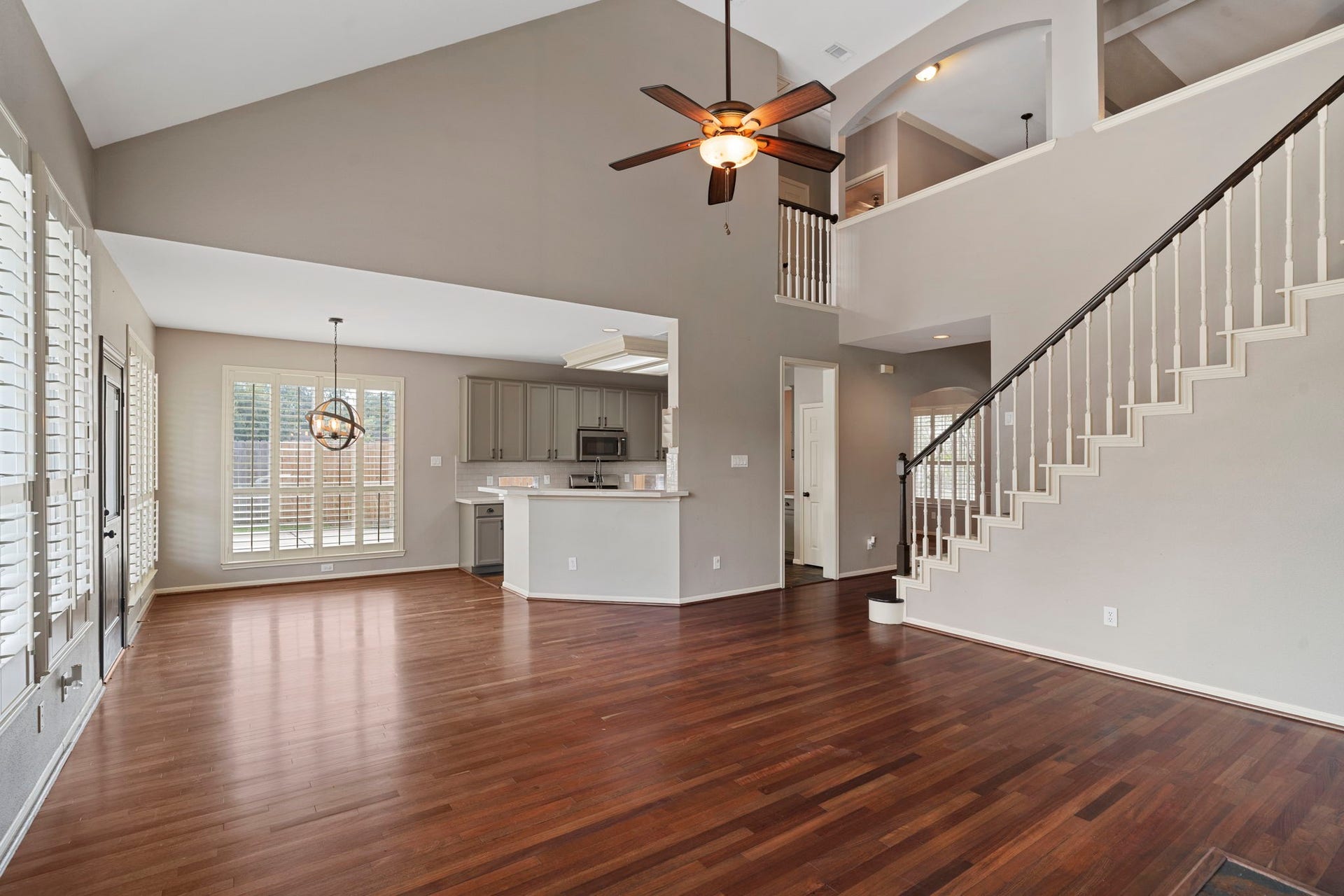 9730 Harrison Lane, Missouri City, TX 77459 Open-concept living room shot looking toward the gourmet kitchen and breakfast nook, illustrating the high vaulted ceilings, custom plantation shutters, overhead ceiling fan, and spacious layout.