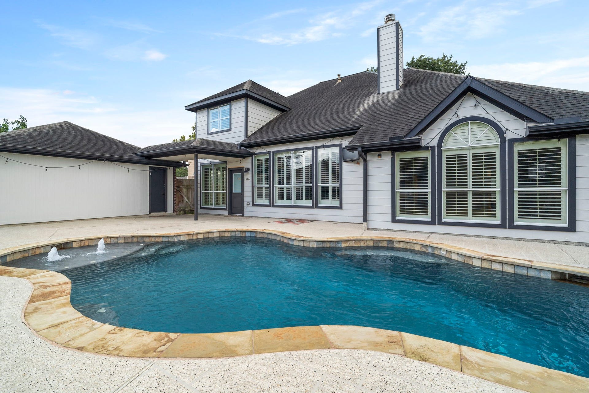 9730 Harrison Lane, Missouri City, TX 77459 Sparkling freeform pool showcase featuring built-in bubbler jets, travertine-style stone coping, and direct view of the rear home exterior and covered patio.