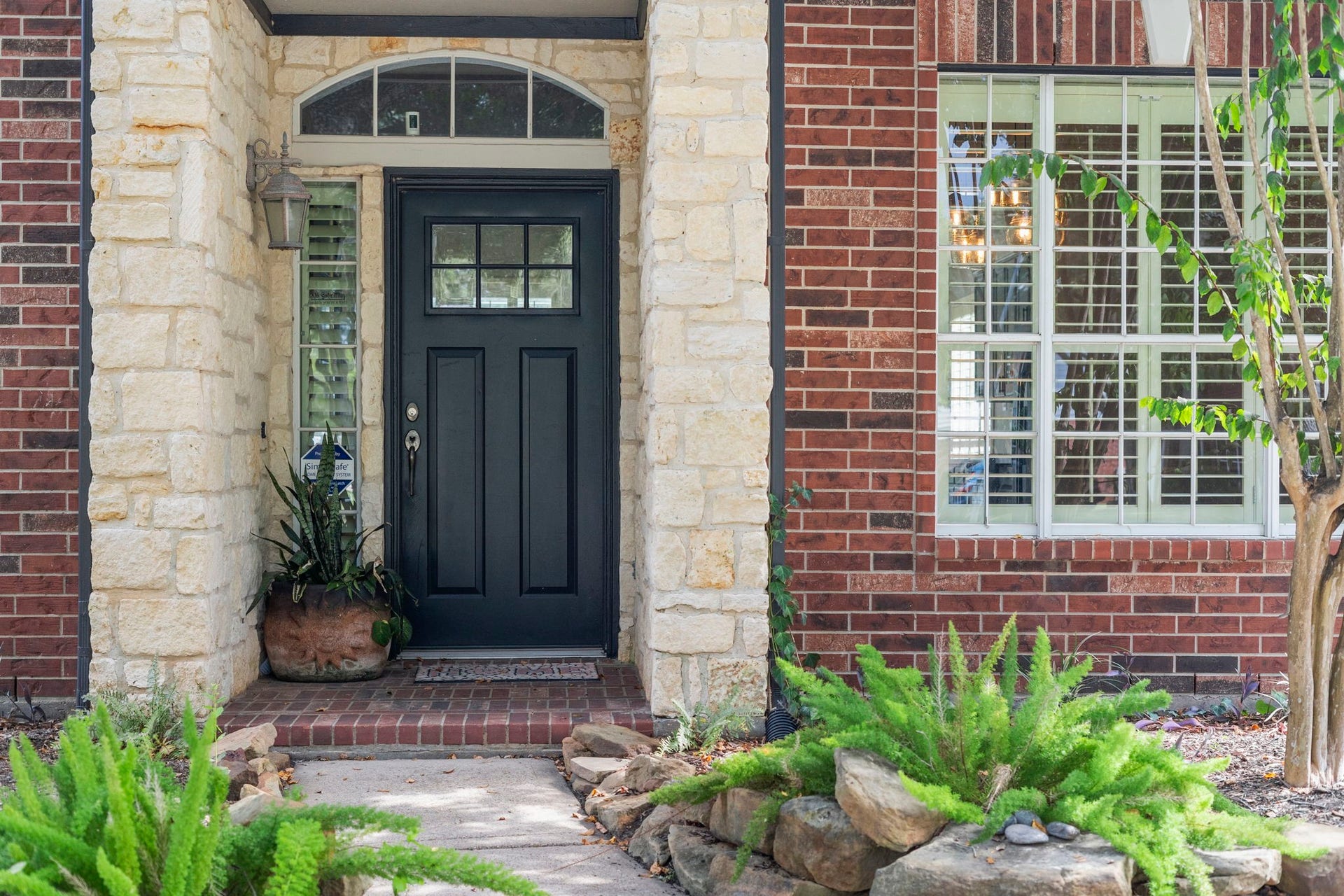 9730 Harrison Lane, Missouri City, TX 77459 Inviting covered entry featuring a classic black front door, stone and brick exterior, and lush landscaping
