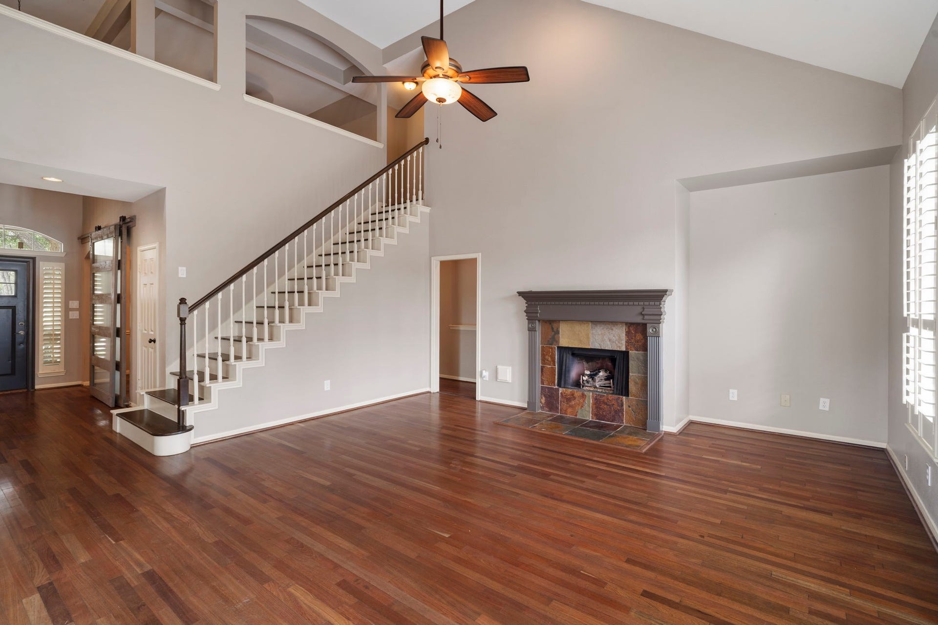 9730 Harrison Lane, Missouri City, TX 77459 Panoramic perspective of the vaulted living room displaying the open second-floor overlook, grand fireplace mantle, dark wood-look floors, and seamless room transitions.