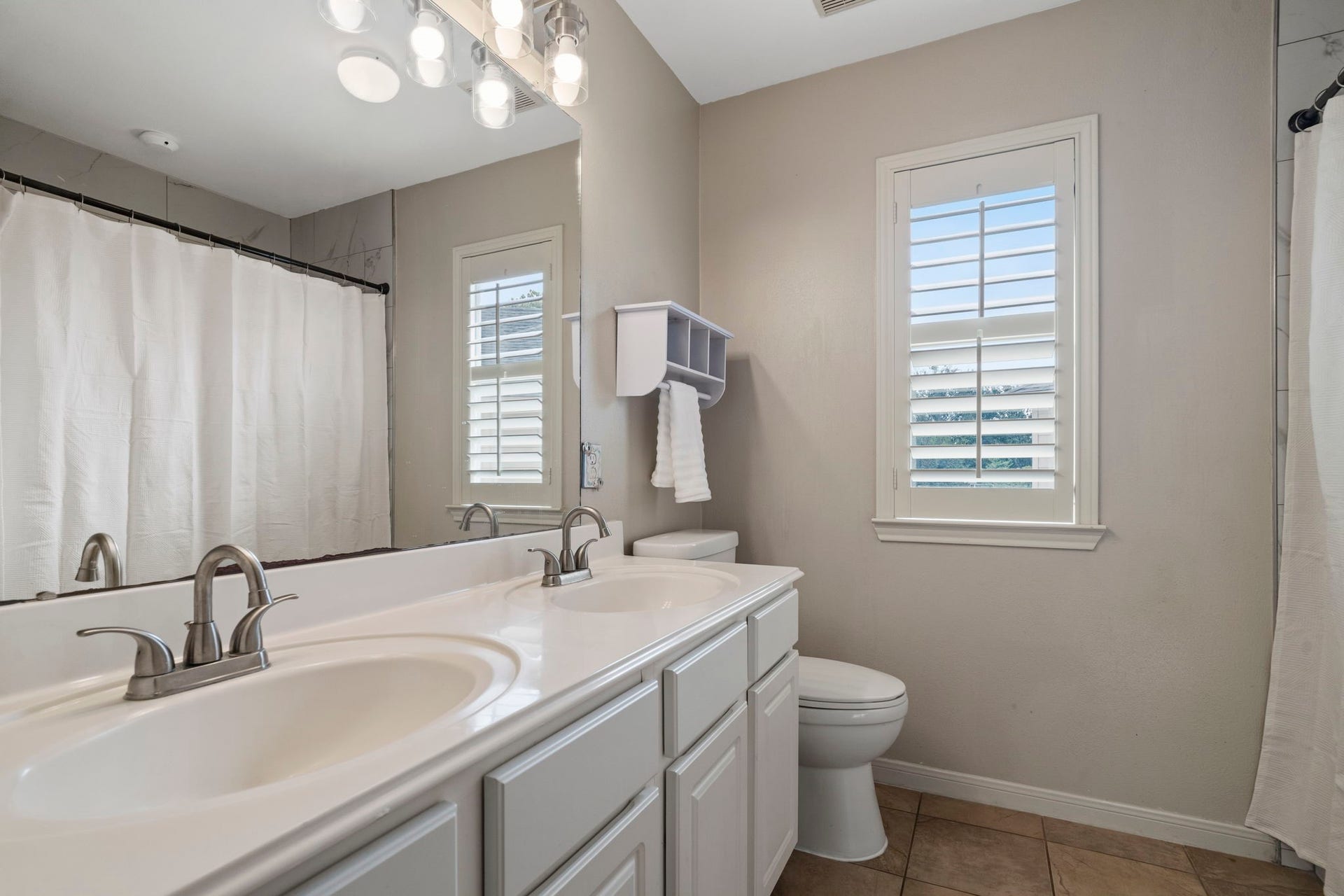 9730 Harrison Lane, Missouri City, TX 77459 Upper-level guest bathroom equipped with a double vanity countertop, upgraded brushed nickel plumbing fixtures, tile flooring, and custom plantation shutters.