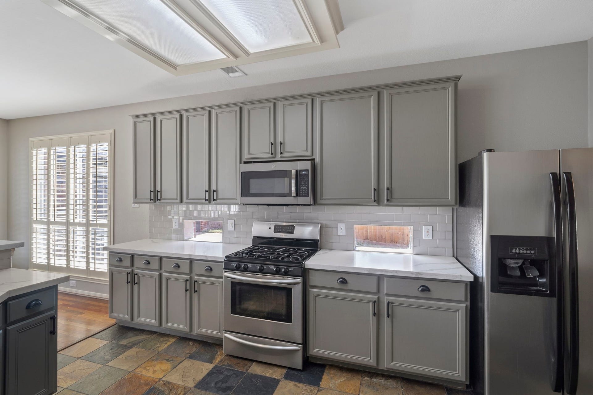 9730 Harrison Lane, Missouri City, TX 77459 Kitchen detail shot featuring soft sage upper and lower cabinets, subway tile backsplash, gas range cooktop with overhead microwave, quartz counters, slate tile floors, and full stainless refrigerator.