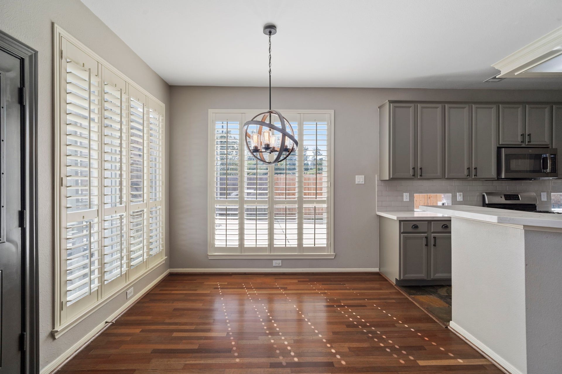 9730 Harrison Lane, Missouri City, TX 77459 Dedicated breakfast dining space highlighting the dual shuttered windows, rustic orb chandelier fixture, wood-look floors, and open breakfast bar counter transition.