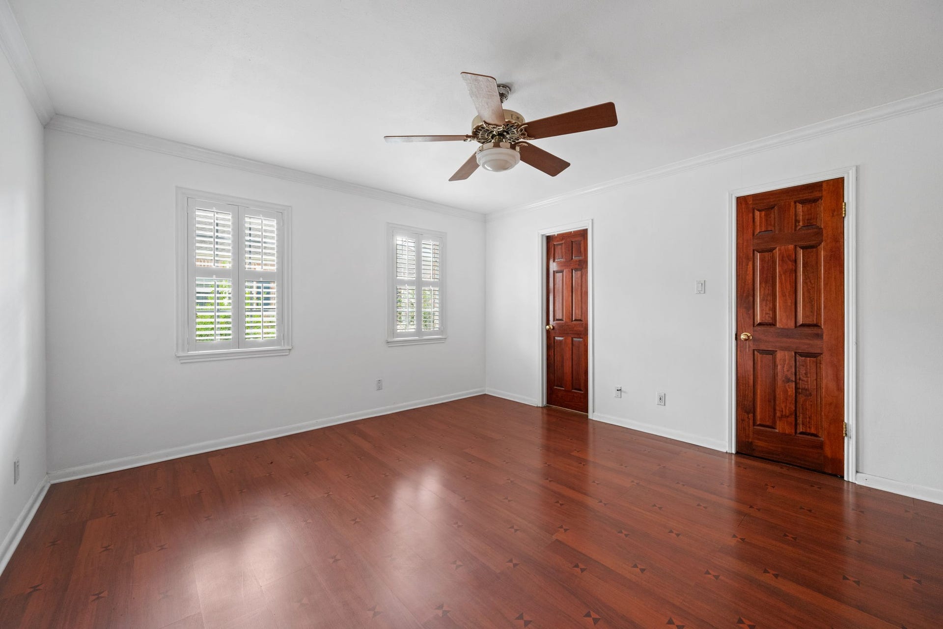 5819 Valley Forge Drive, #91, Houston, TX 77057 Bright and spacious room featuring rich hardwood floors, two wooden doors, and large windows with shutters, complemented by a ceiling fan.