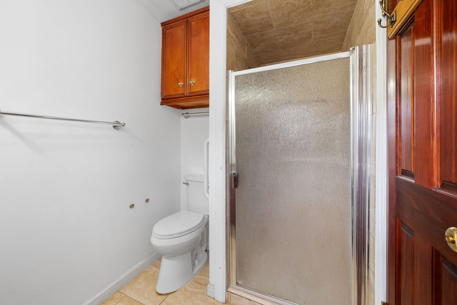 5819 Valley Forge Drive, #91, Houston, TX 77057 Cozy bathroom featuring a walk-in shower with frosted glass door, elegant wooden cabinetry, and a classic white toilet.