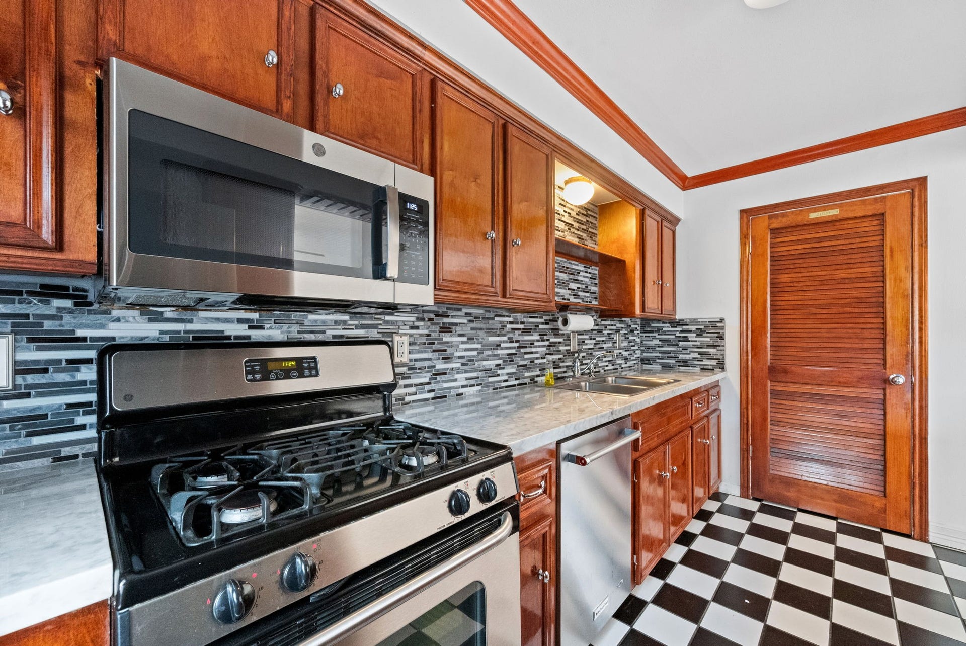 5819 Valley Forge Drive, #91, Houston, TX 77057 Stylish kitchen featuring modern stainless steel appliances, a sleek tile backsplash, rich wood cabinetry, and classic black-and-white checkered flooring for a timeless appeal.