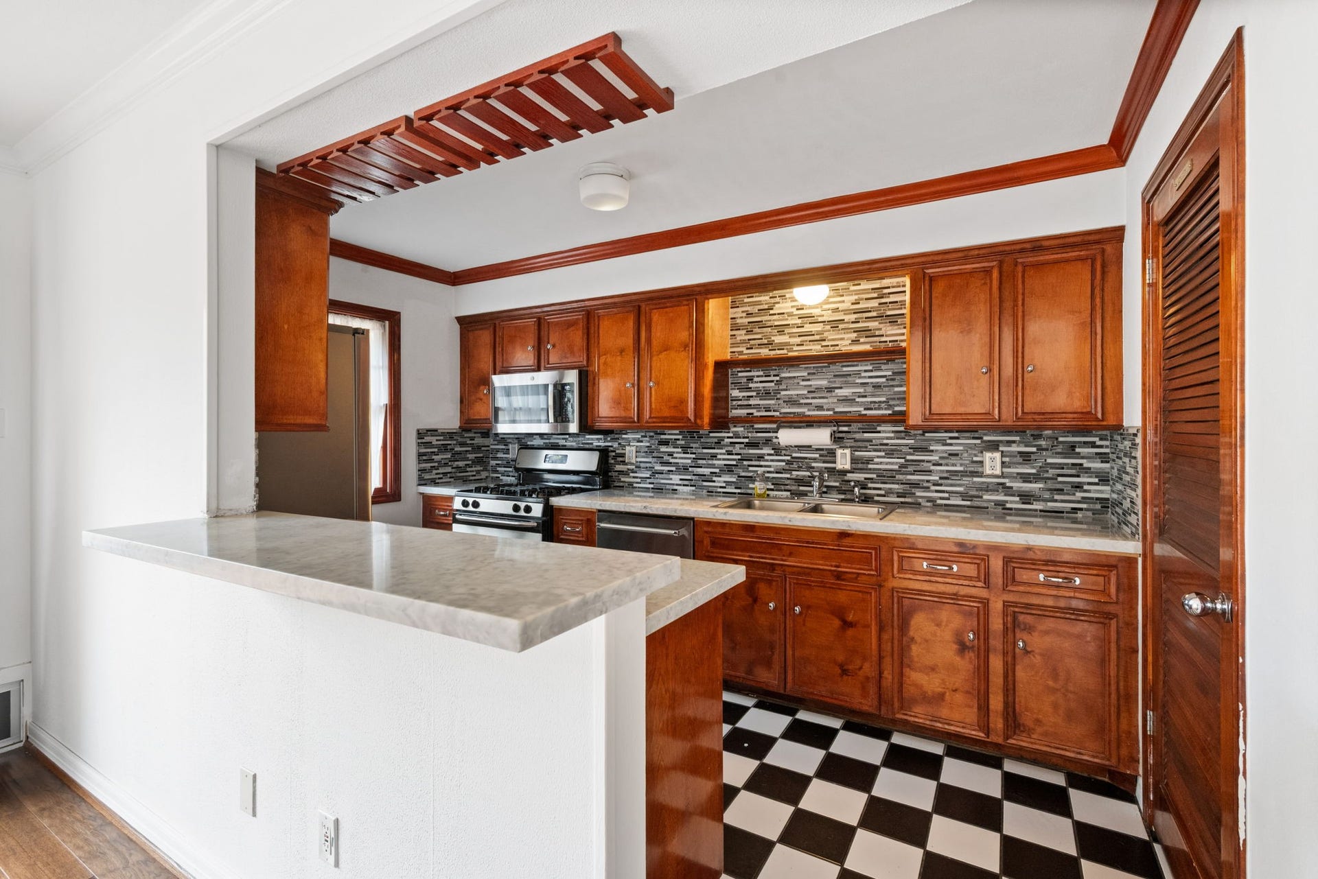 5819 Valley Forge Drive, #91, Houston, TX 77057 Charming kitchen featuring warm wooden cabinetry, modern stainless steel appliances, and a stylish mosaic backsplash, complemented by a classic black-and-white checkered floor.