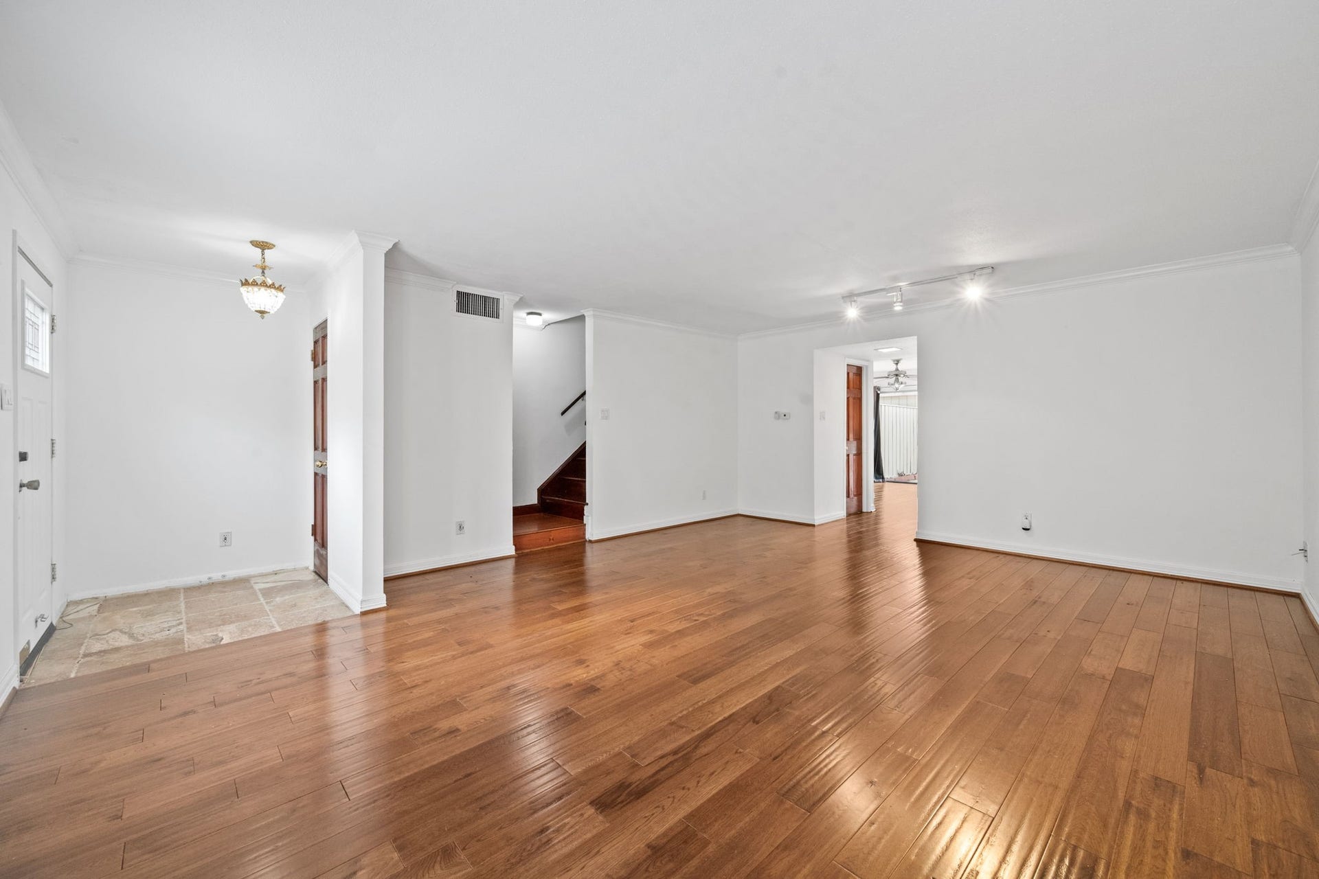 5819 Valley Forge Drive, #91, Houston, TX 77057 Spacious living area with elegant hardwood floors and bright white walls, featuring recessed lighting and a charming chandelier, leading to a staircase and additional rooms.