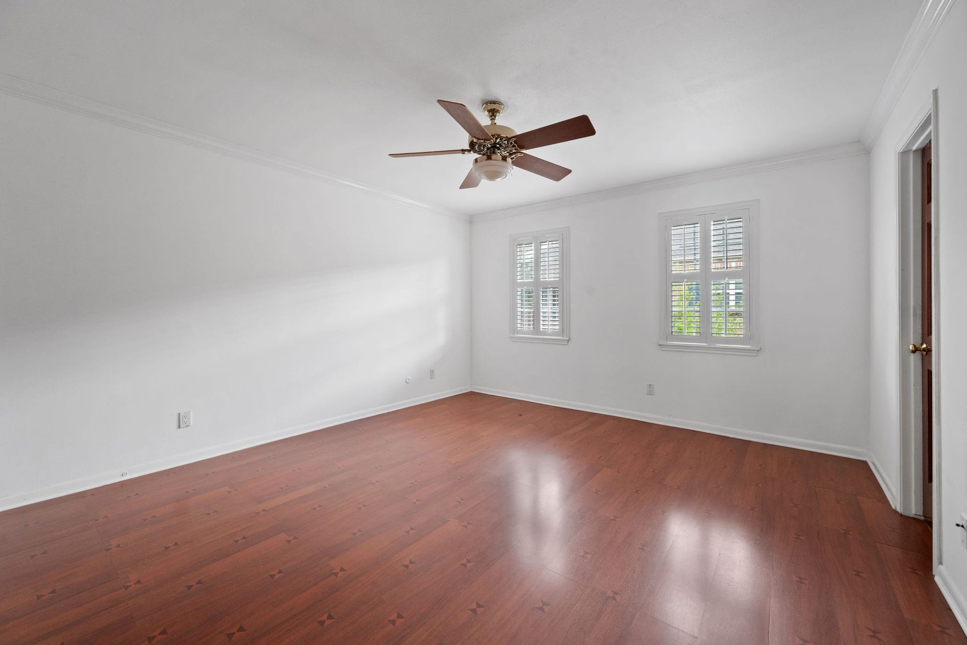 5819 Valley Forge Drive, #91, Houston, TX 77057 Spacious bedroom with rich hardwood floors, elegant white walls, and abundant natural light from dual windows with plantation shutters. Features a ceiling fan for added comfort.