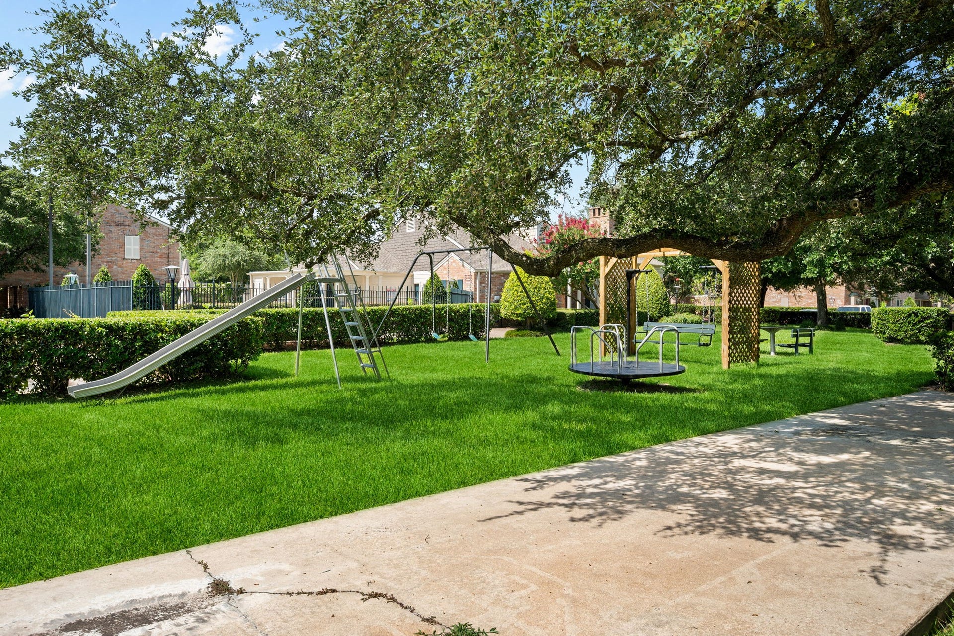 5819 Valley Forge Drive, #91, Houston, TX 77057 Charming backyard oasis featuring a well-maintained playground with a slide and merry-go-round, surrounded by lush greenery and mature trees, perfect for family fun.