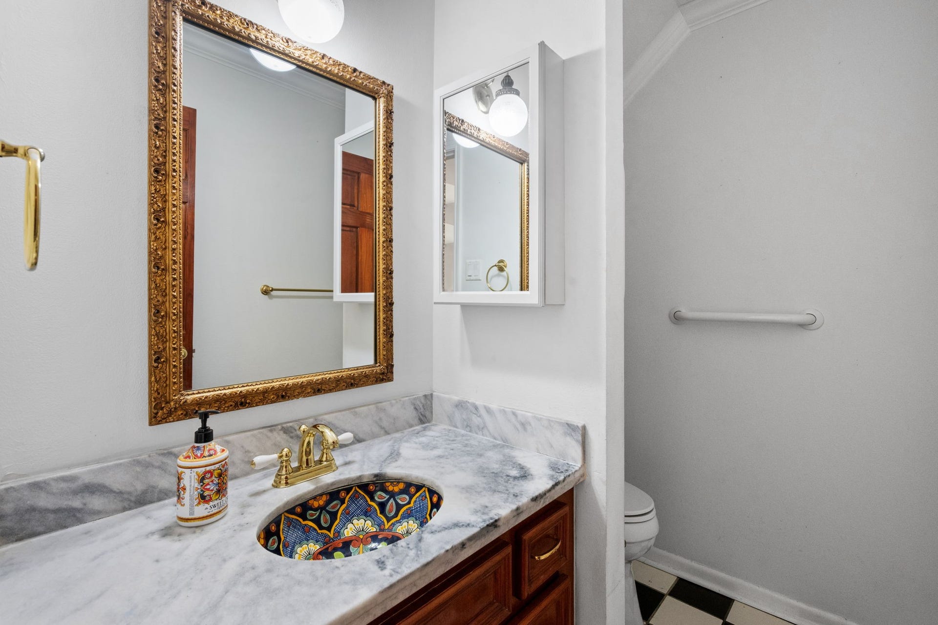 5819 Valley Forge Drive, #91, Houston, TX 77057 Elegant bathroom featuring a marble countertop with a colorful mosaic sink, ornate gold-framed mirror, and classic black-and-white checkered flooring.