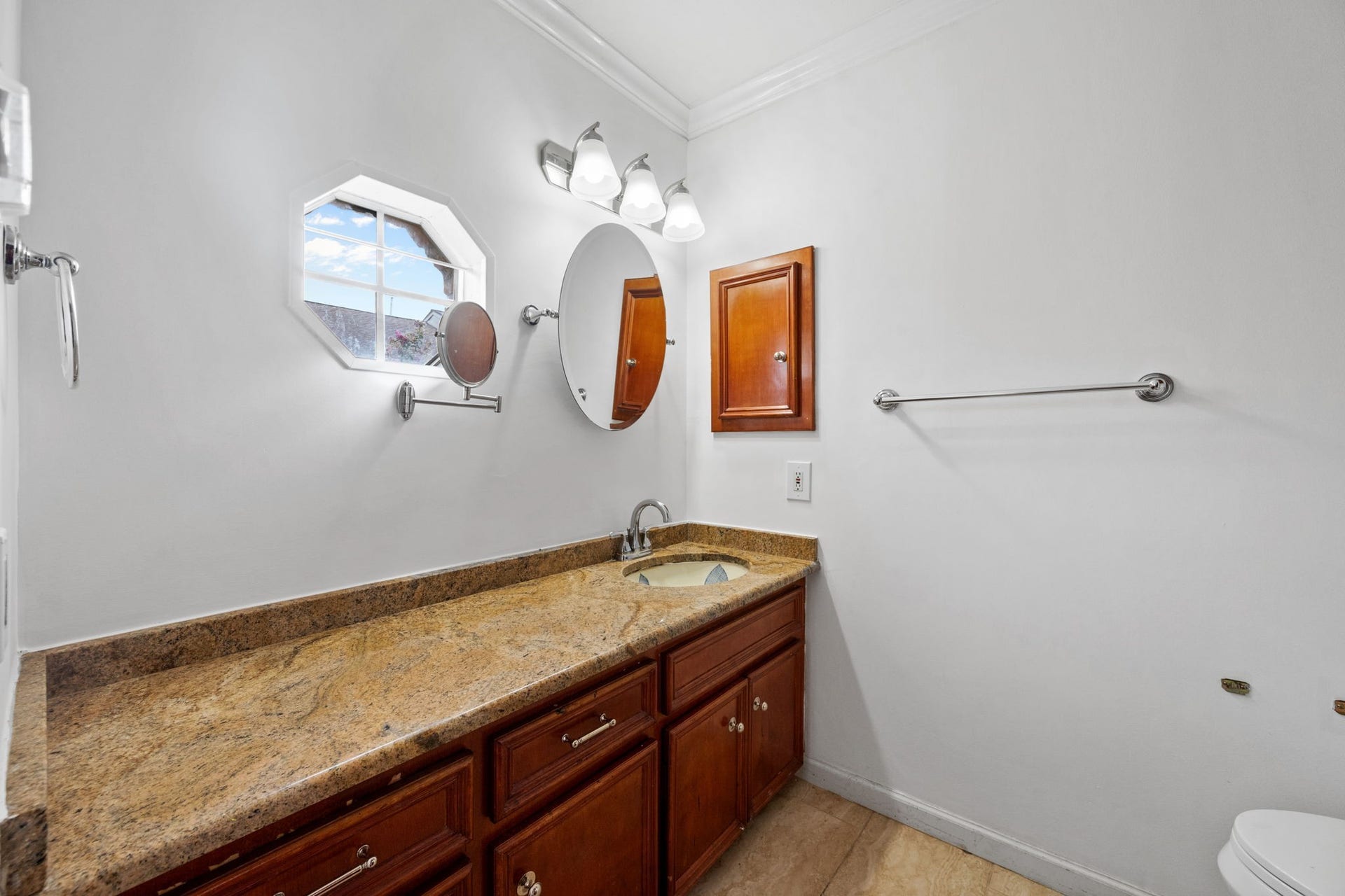 5819 Valley Forge Drive, #91, Houston, TX 77057 Elegant bathroom featuring a spacious granite countertop with rich wood cabinetry, complemented by a stylish octagonal window and modern lighting fixtures.
