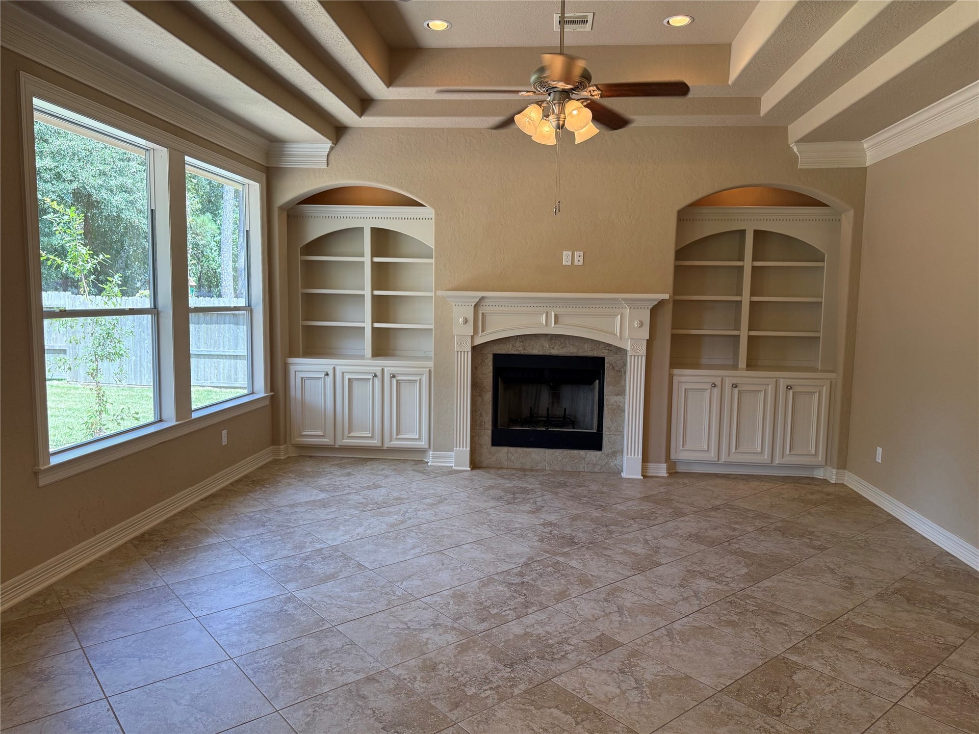 19841 S Plantation Estates Drive, Porter, TX 77365 Elegant living room featuring a cozy fireplace flanked by custom built-in shelves, recessed ceiling with a fan, and large windows offering abundant natural light.