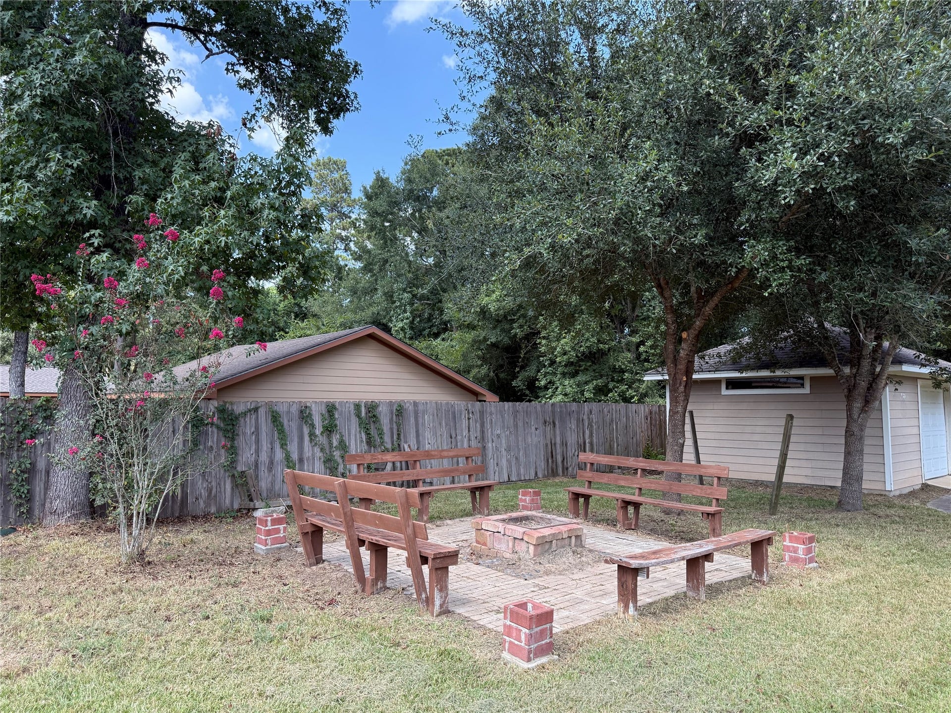19841 S Plantation Estates Drive, Porter, TX 77365 Charming backyard with a cozy brick fire pit, surrounded by wooden benches and shaded by mature trees, perfect for outdoor gatherings.