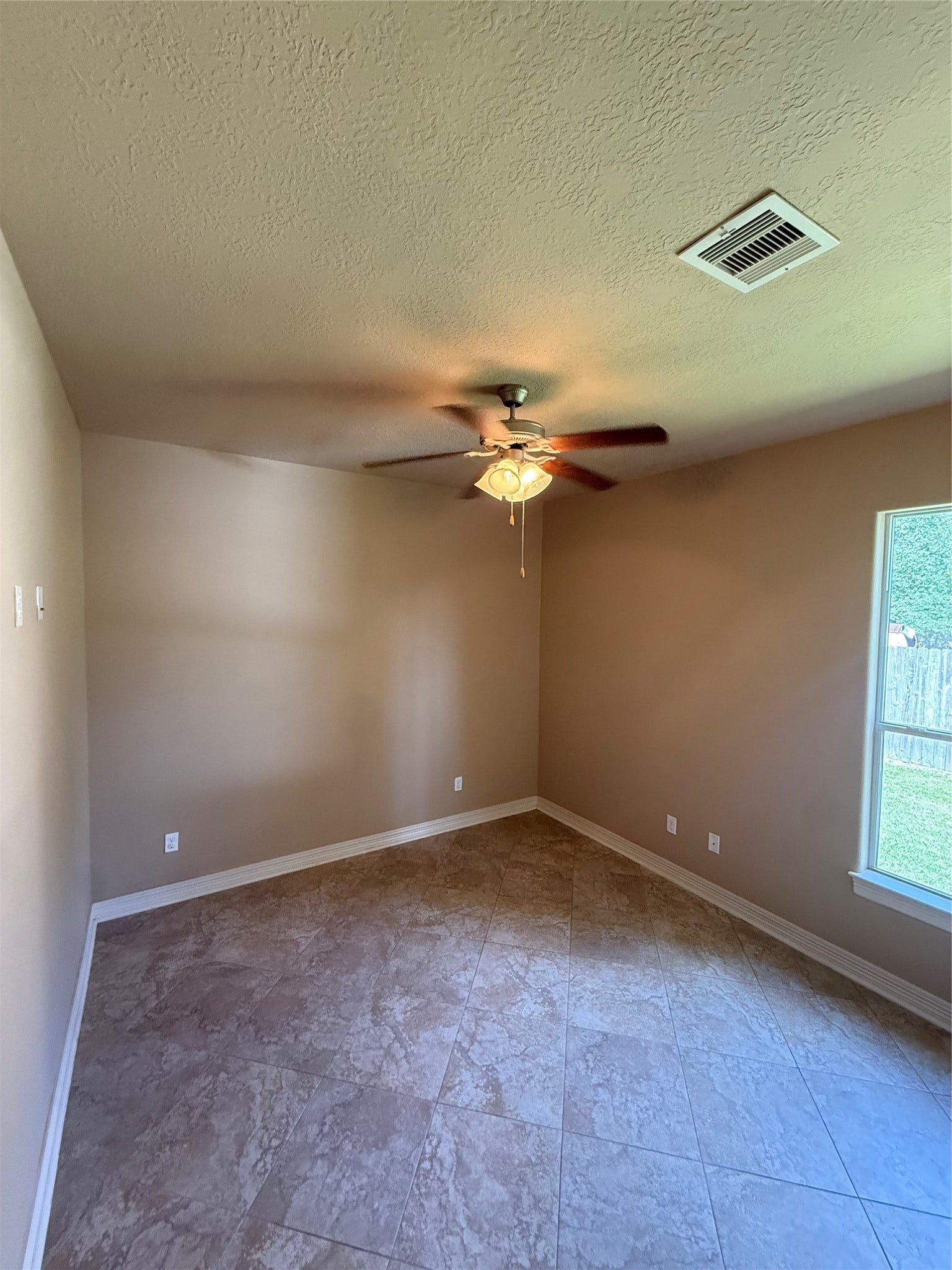 19841 S Plantation Estates Drive, Porter, TX 77365 Cozy room featuring tiled flooring, a ceiling fan, and a large window offering natural light and a view of the fenced backyard.